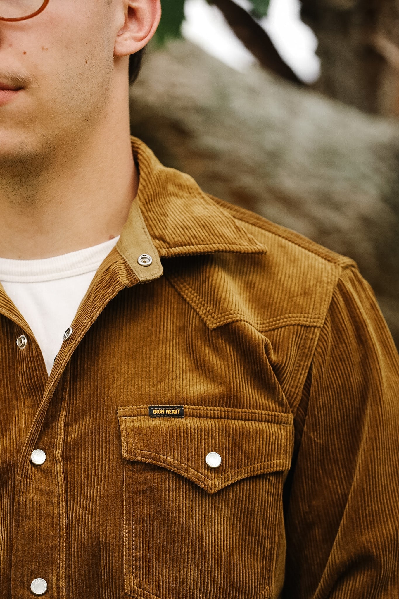 Close-up of a brown corduroy shirt and blue jeans with a blurred background