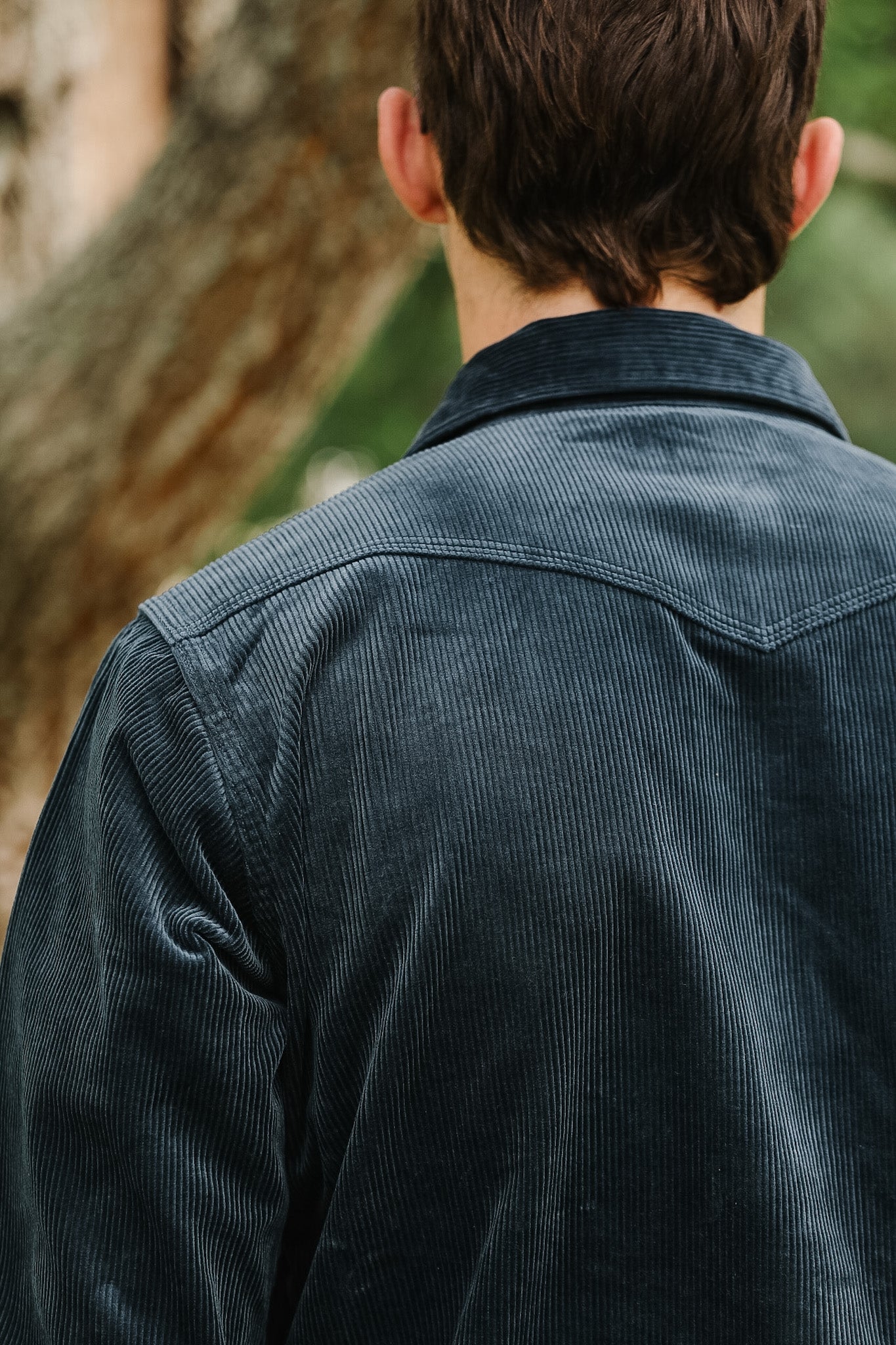 Close-up of a hand buttoning a dark blue corduroy jacket.