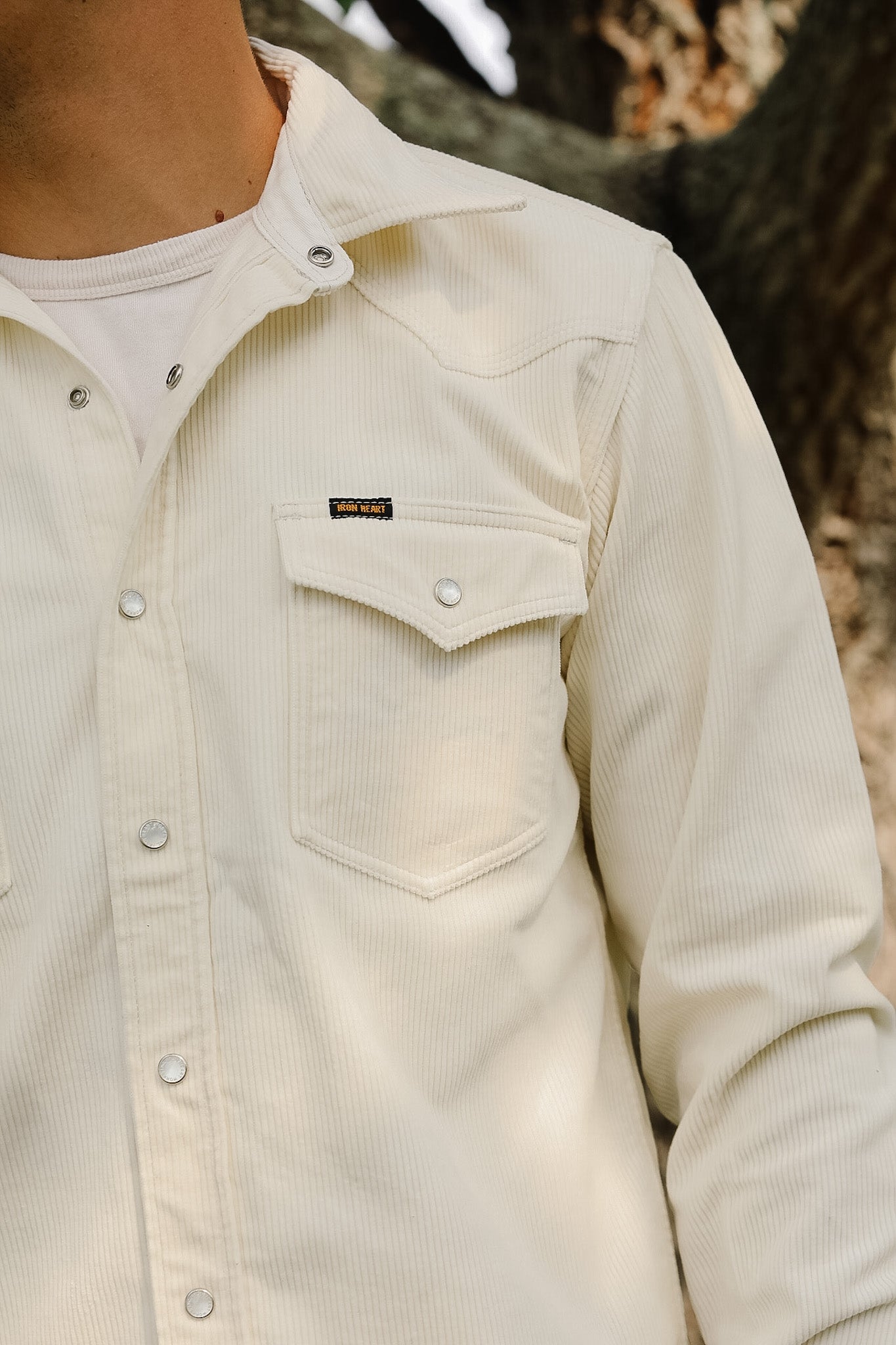 Close-up of a beige corduroy shirt with a brand label, worn by a person outdoors.
