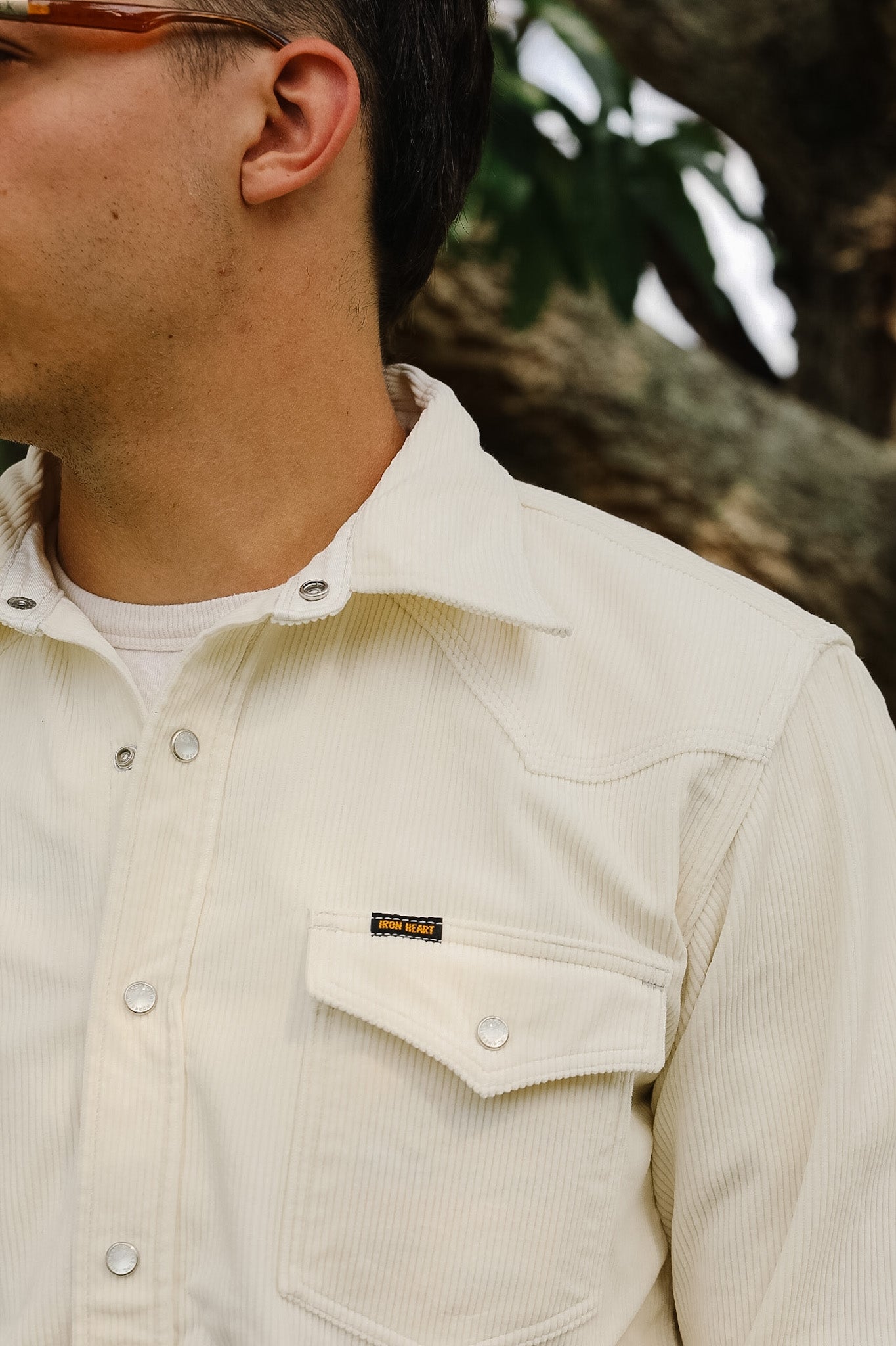 Close-up of a person wearing a beige corduroy shirt with a brand logo.