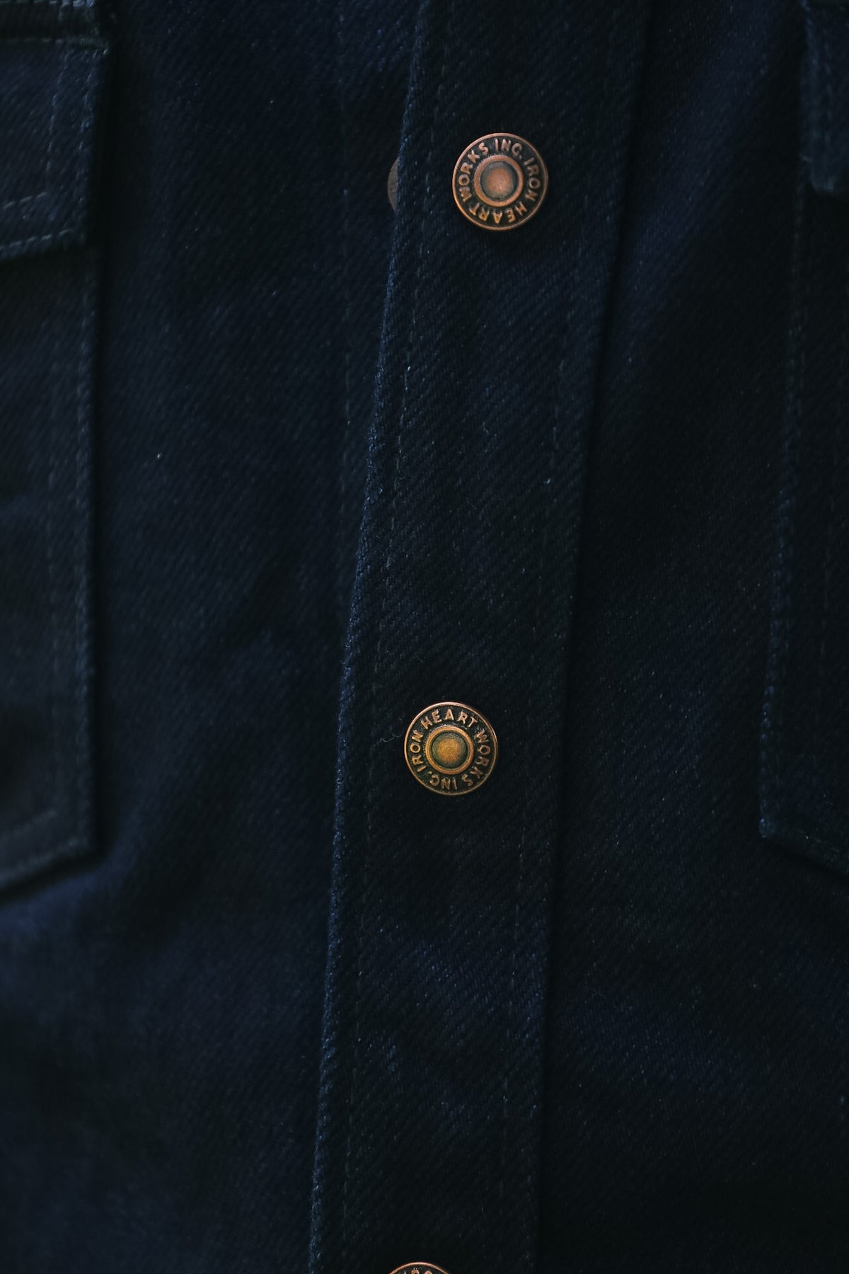 Close-up of a dark navy blue denim jacket showing the button placket with bronze-toned metal buttons.