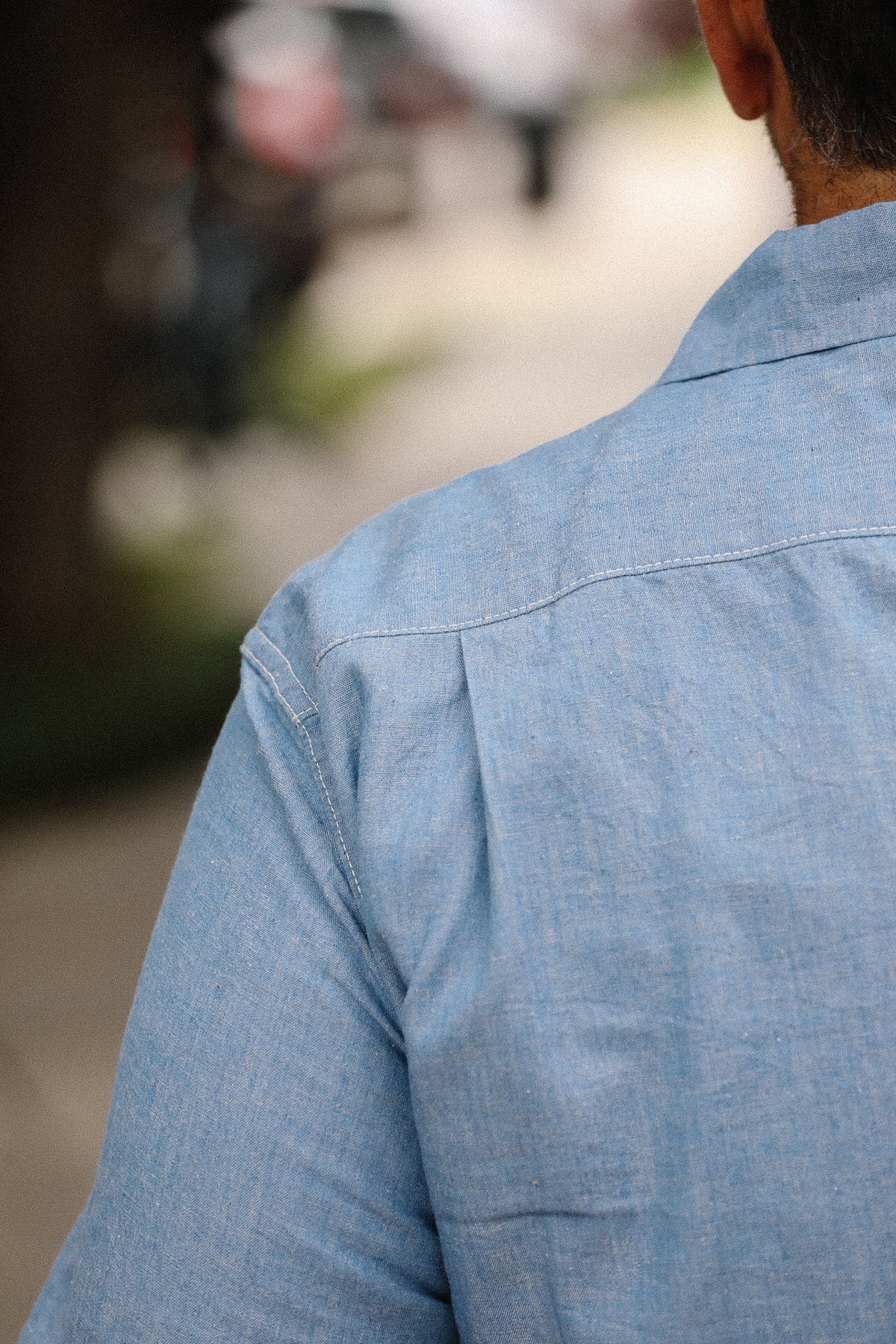 Close-up of a person wearing a blue denim shirt with a blurred background
