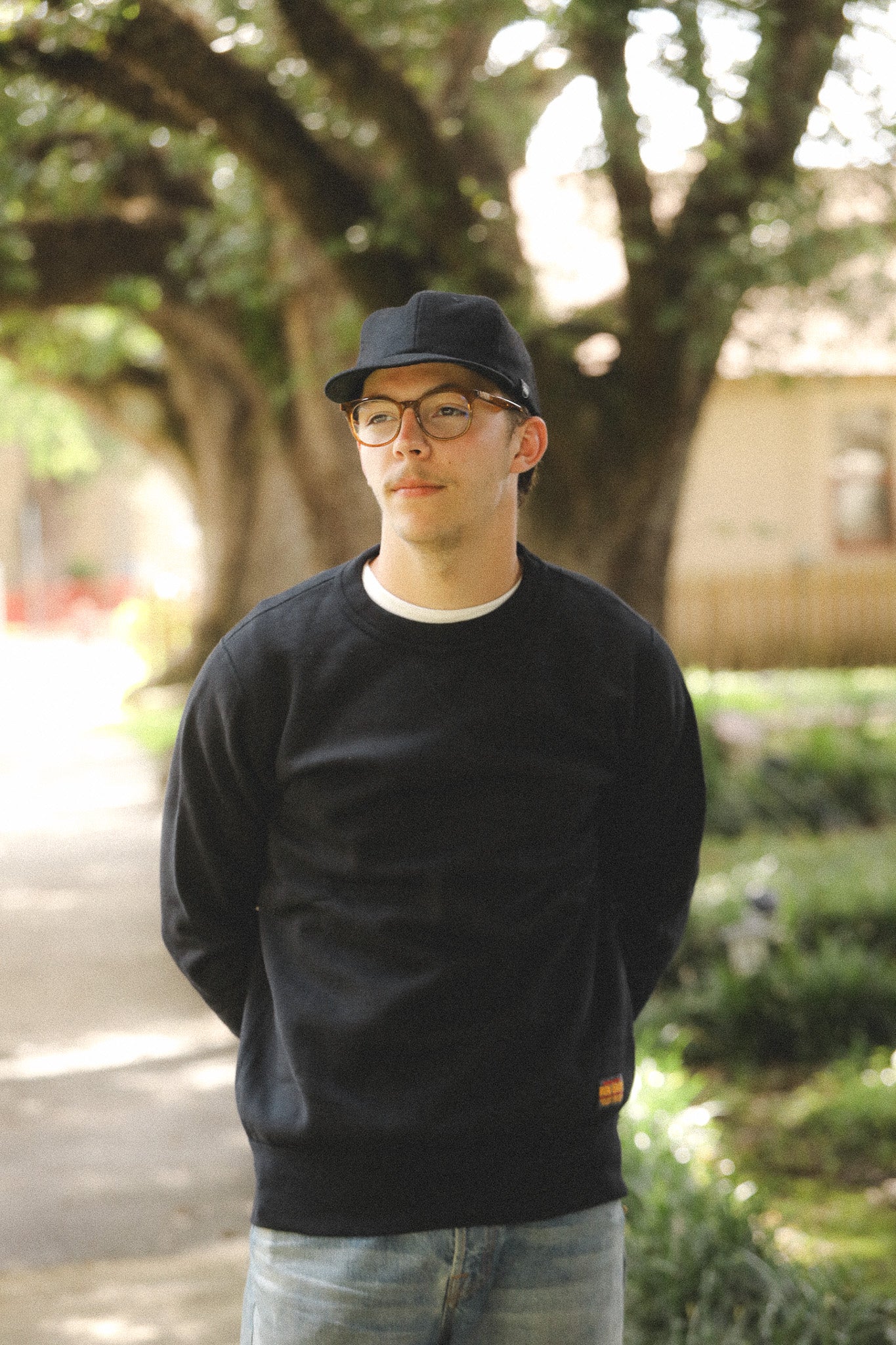 Man wearing a black sweatshirt and cap outdoors with trees and a building in the background