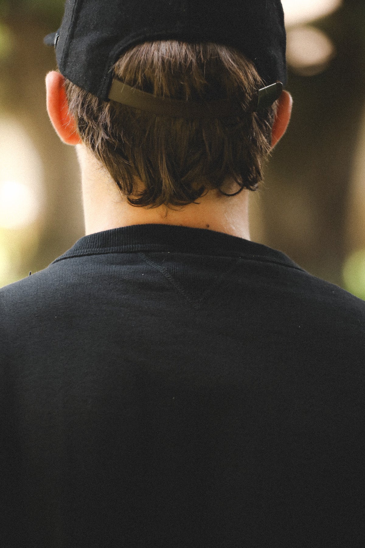 Person wearing a black cap and dark shirt with a blurred natural background