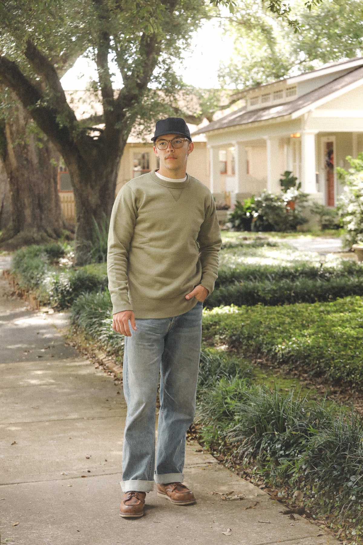 Man standing on a wooden path in a residential area with a house and trees in the background.