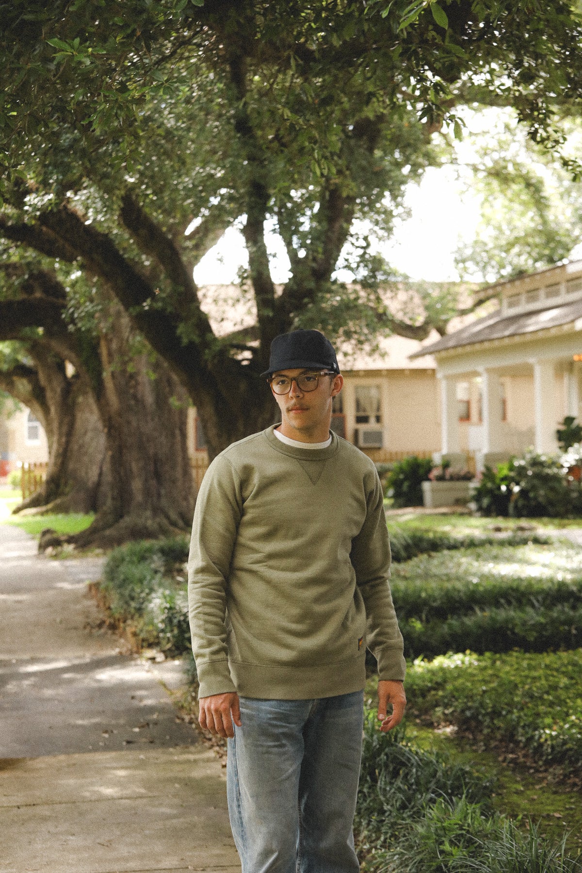 Man standing on a sidewalk with trees and a house in the background