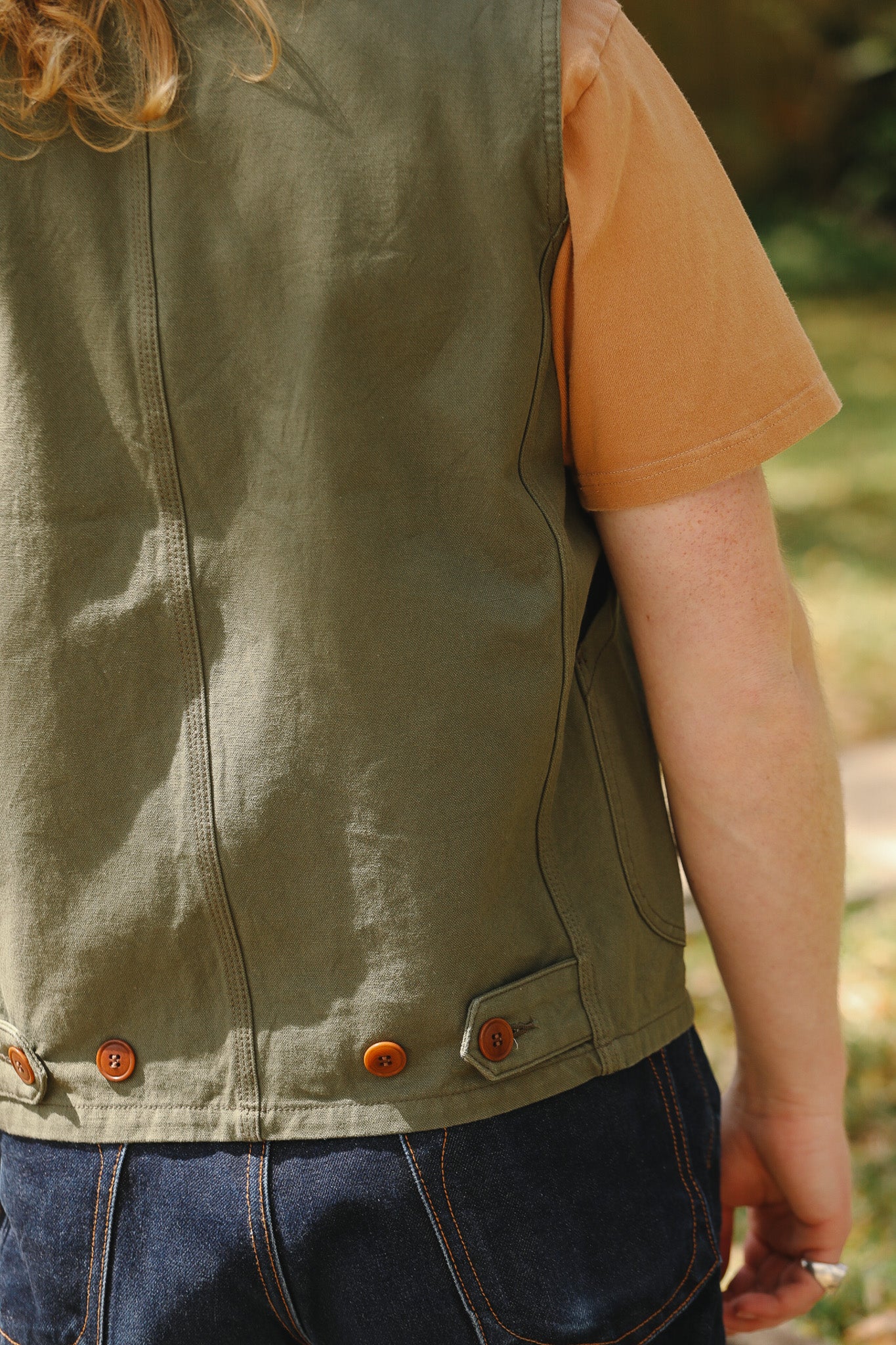 Person wearing a green vest with orange buttons outdoors