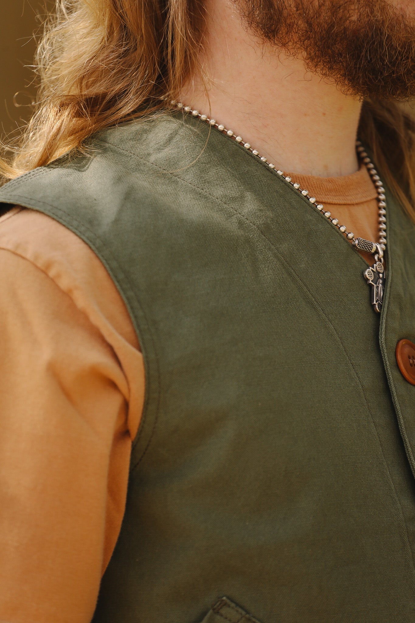 Person wearing a green vest over an orange shirt with a necklace featuring a cross pendant.