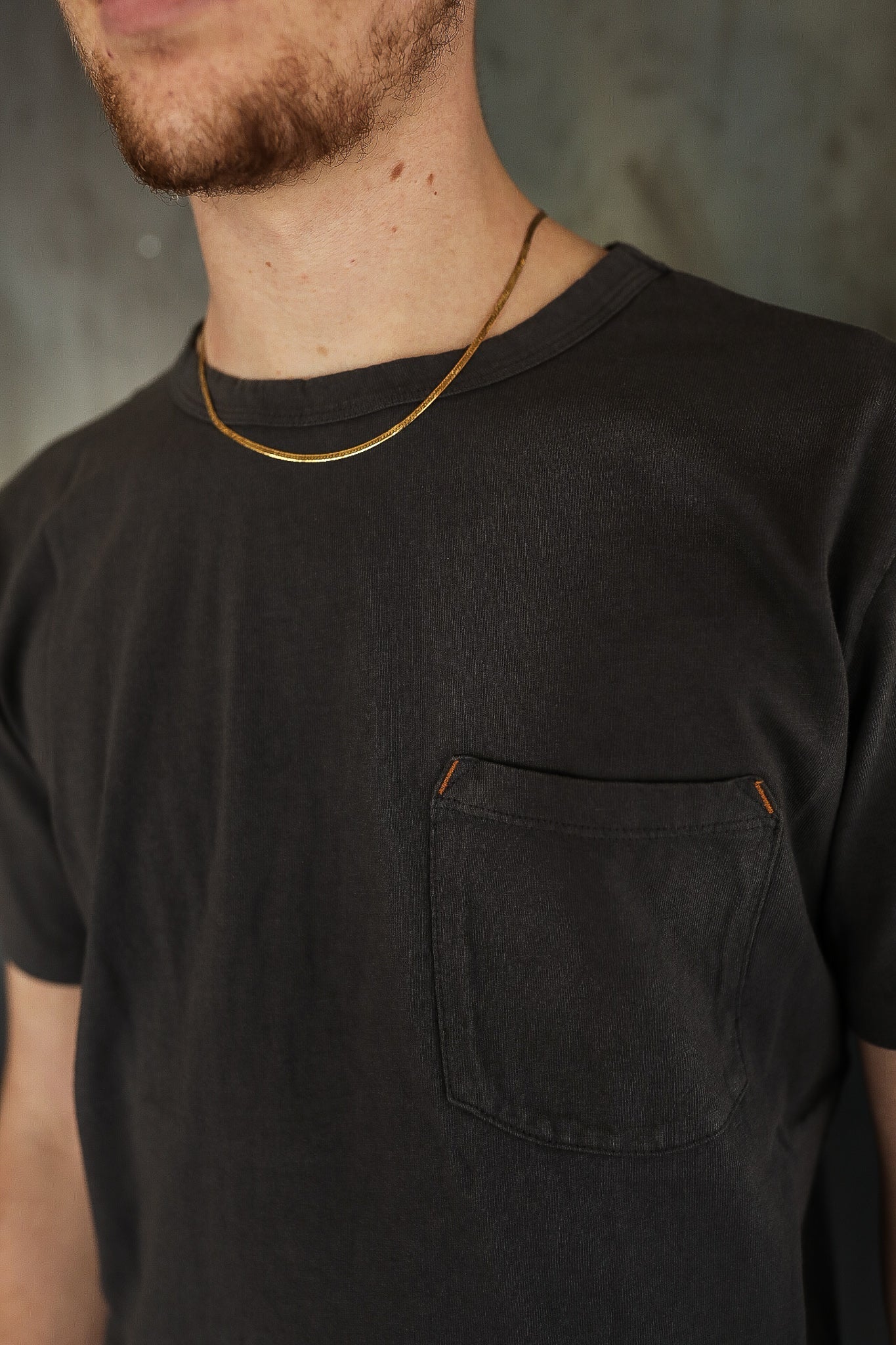 Man wearing black crew neck pocket t-shirt and thin gold chain necklace, close-up