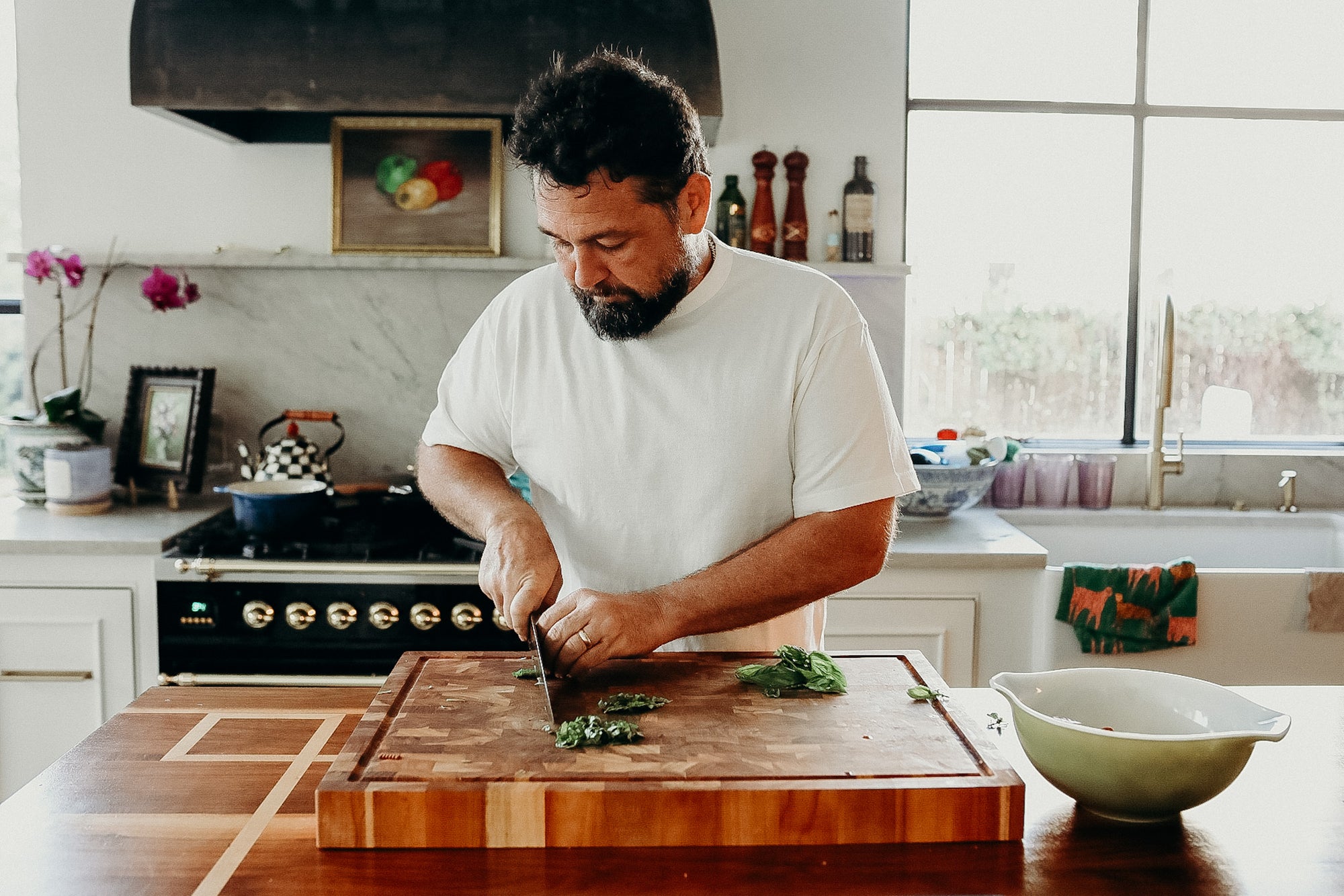 person wearing white loopwheel tee cutting basil in kitchen 