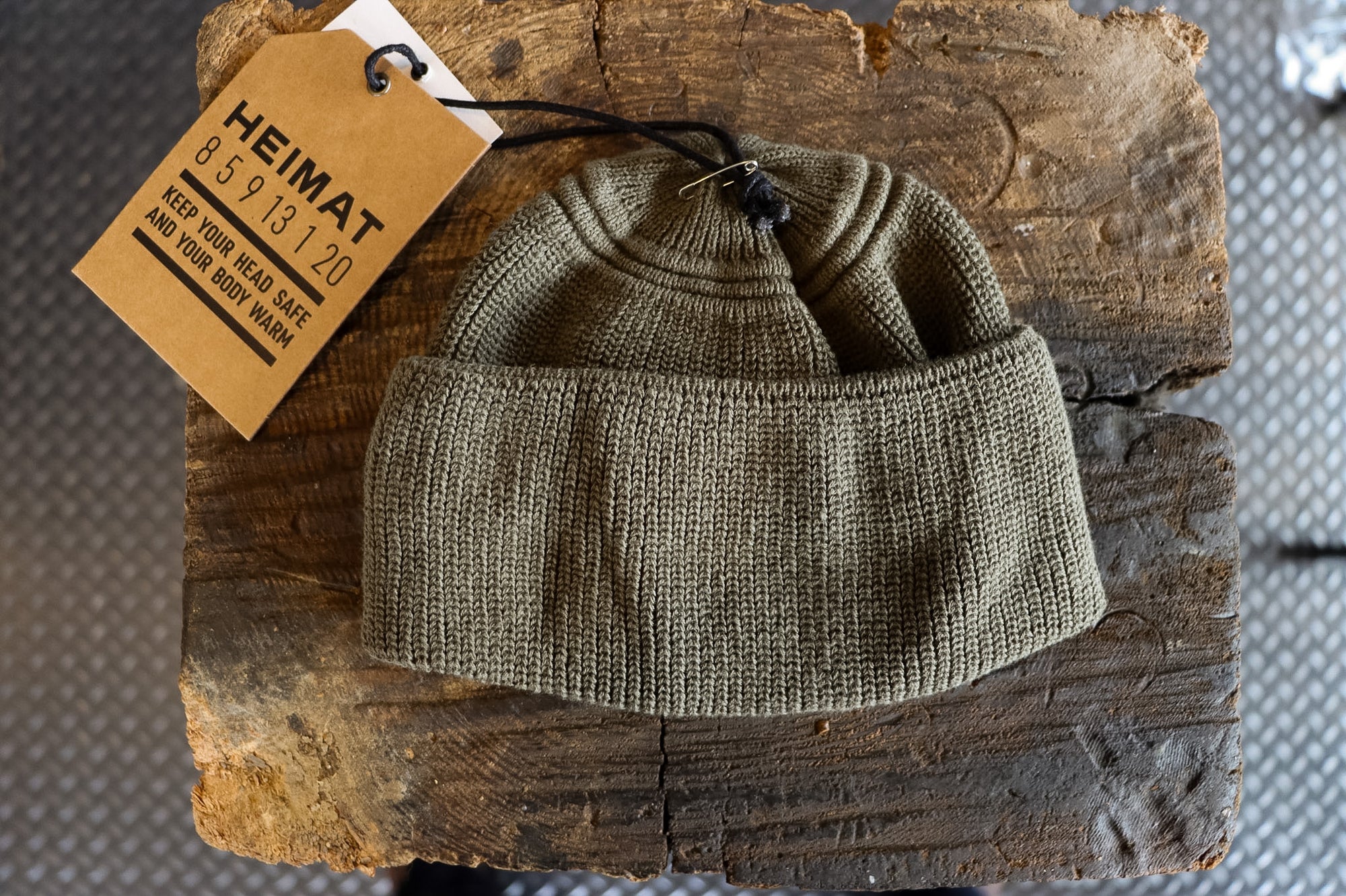 Knitted green beanie on a wooden block with a 'HEIMAT' tag.