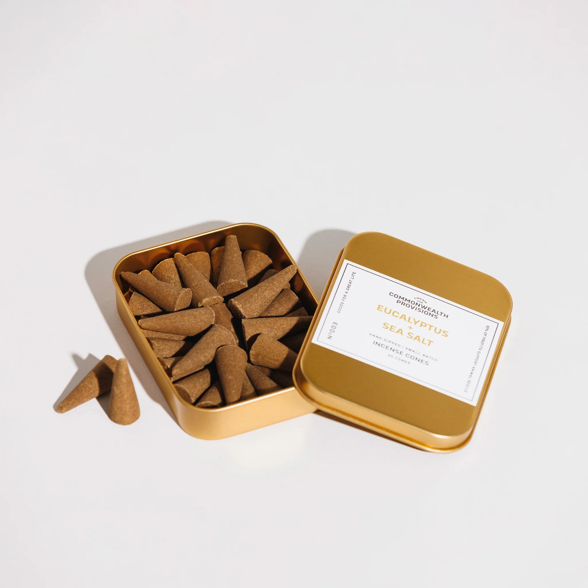 Open gold tin box with eucalyptus and sea salt incense cones inside on white background