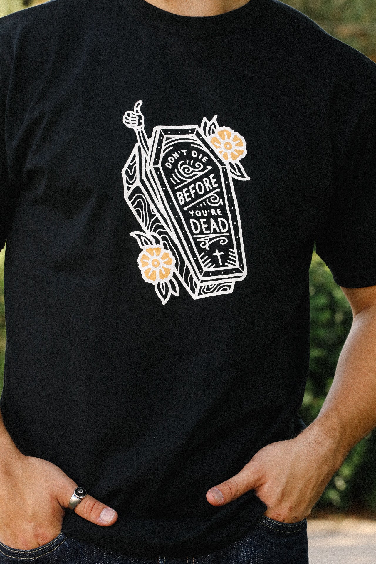 Black T-shirt with white coffin graphic and yellow flowers, text reads 'Don't die before you're dead'