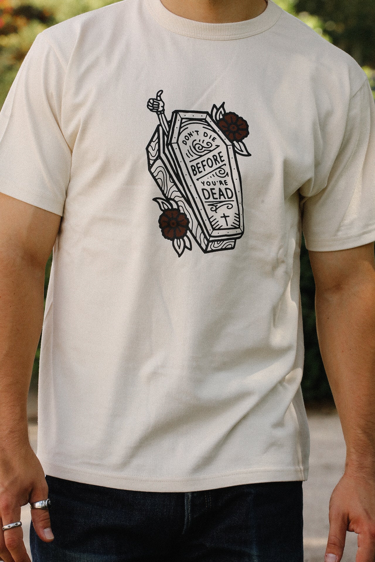 Cream Iron Shop Provisions t-shirt with coffin graphic and text 'Don't die before you're dead' worn by man outdoors