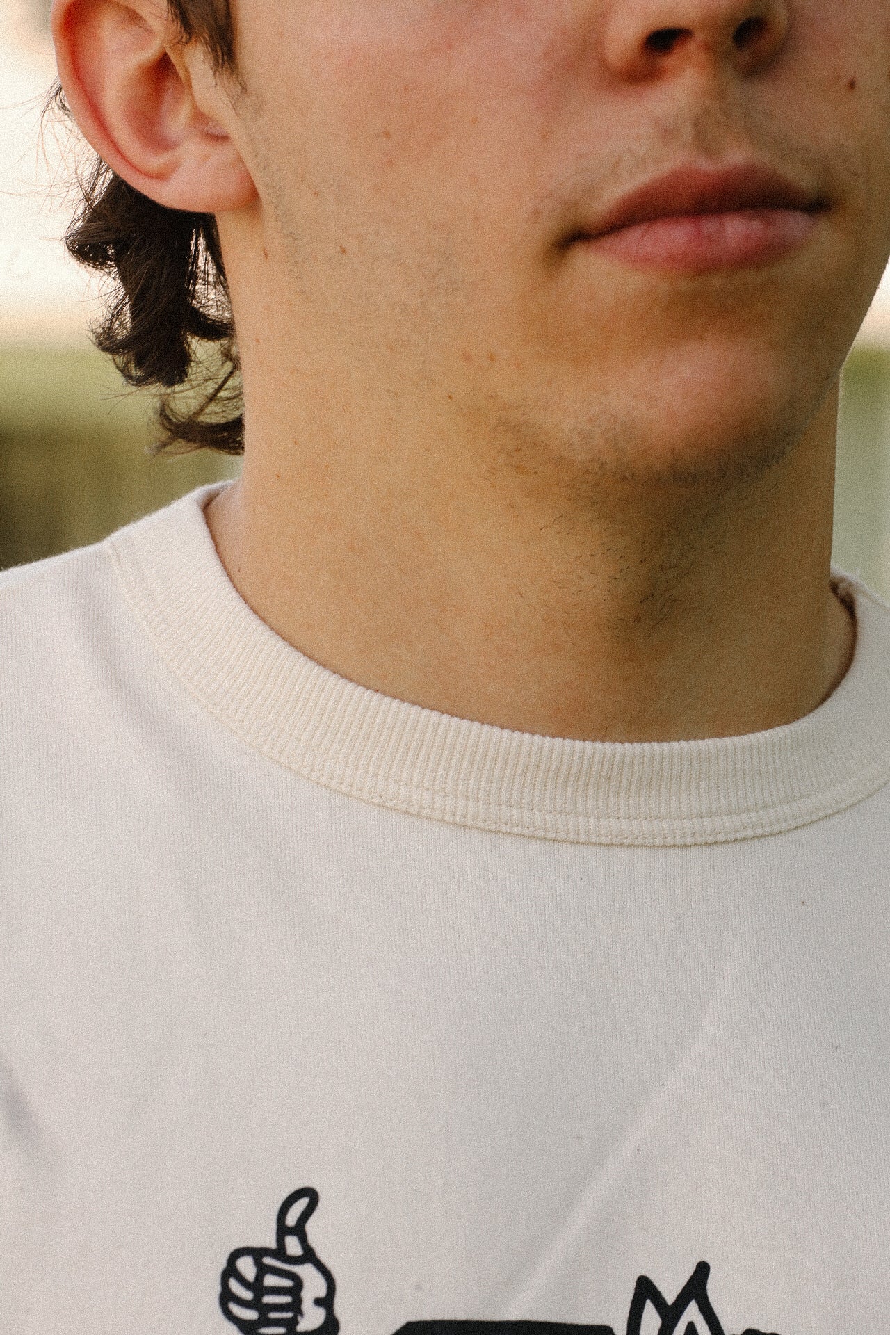 Close-up of a person wearing a cream-colored crew neck t-shirt with a black graphic design. Iron Shop Provisions apparel.