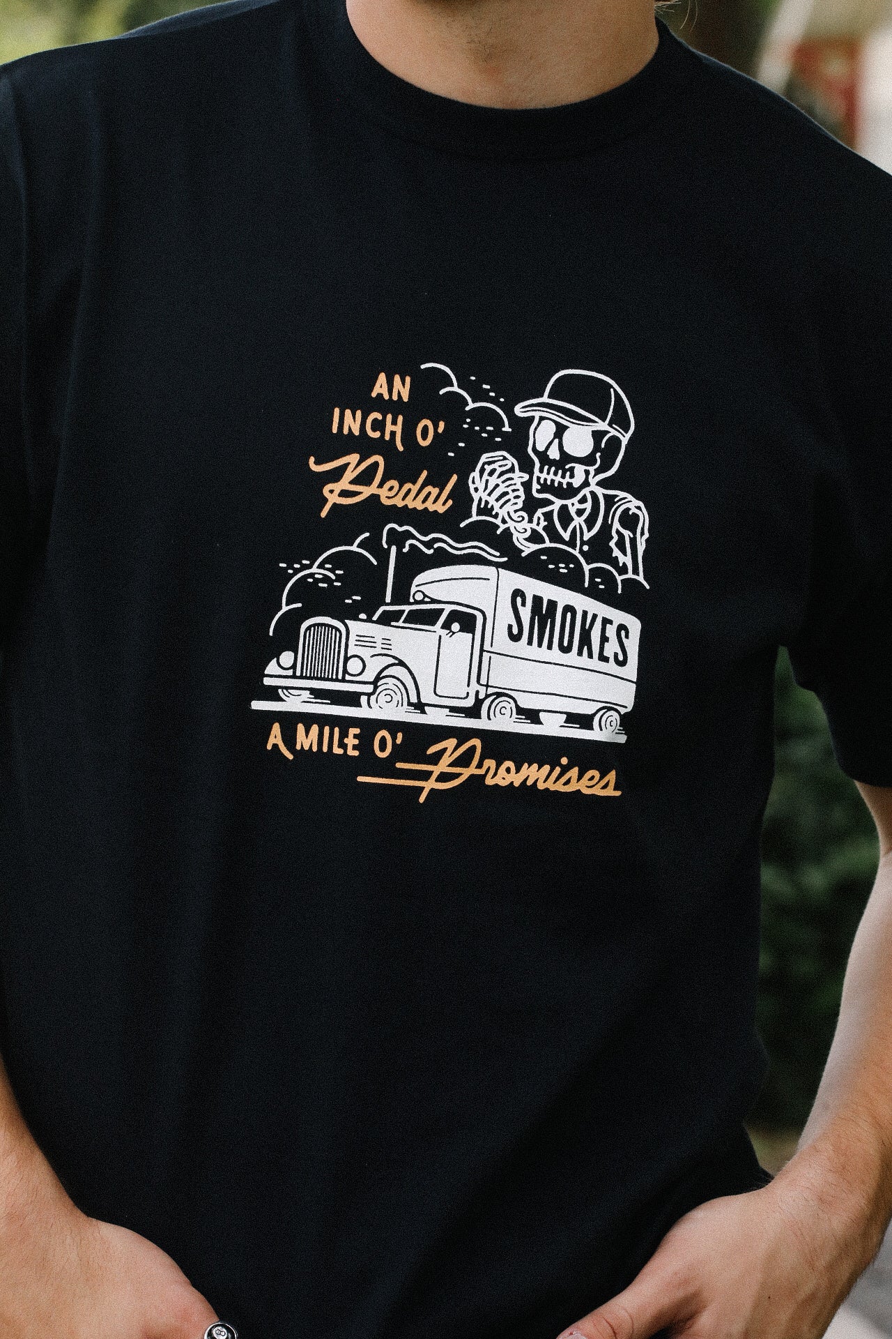Black tee with skeleton driver graphic and vintage truck labeled 'SMOKES' with text An Inch O' Pedal A Mile O' Promises