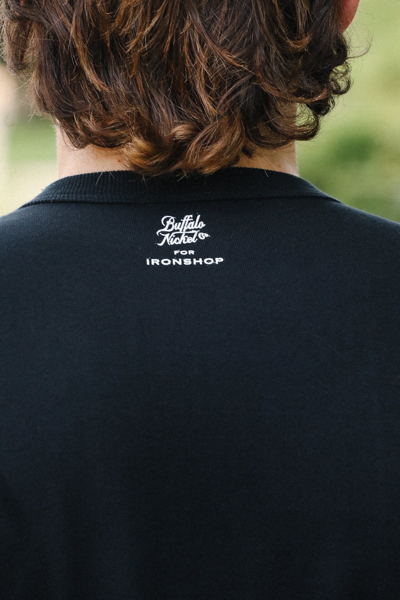 Back view of person wearing a black Iron Shop Provisions tee with white Buffalo Nickel logo on neck