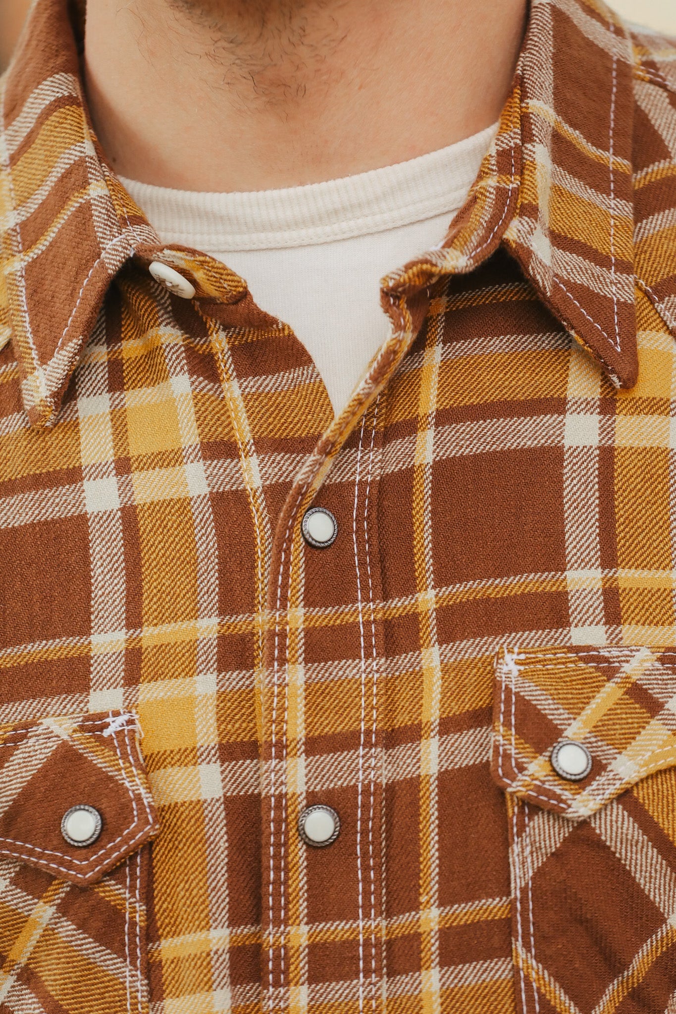 Close-up of a brown and yellow plaid shirt with a focus on the collar and buttons.