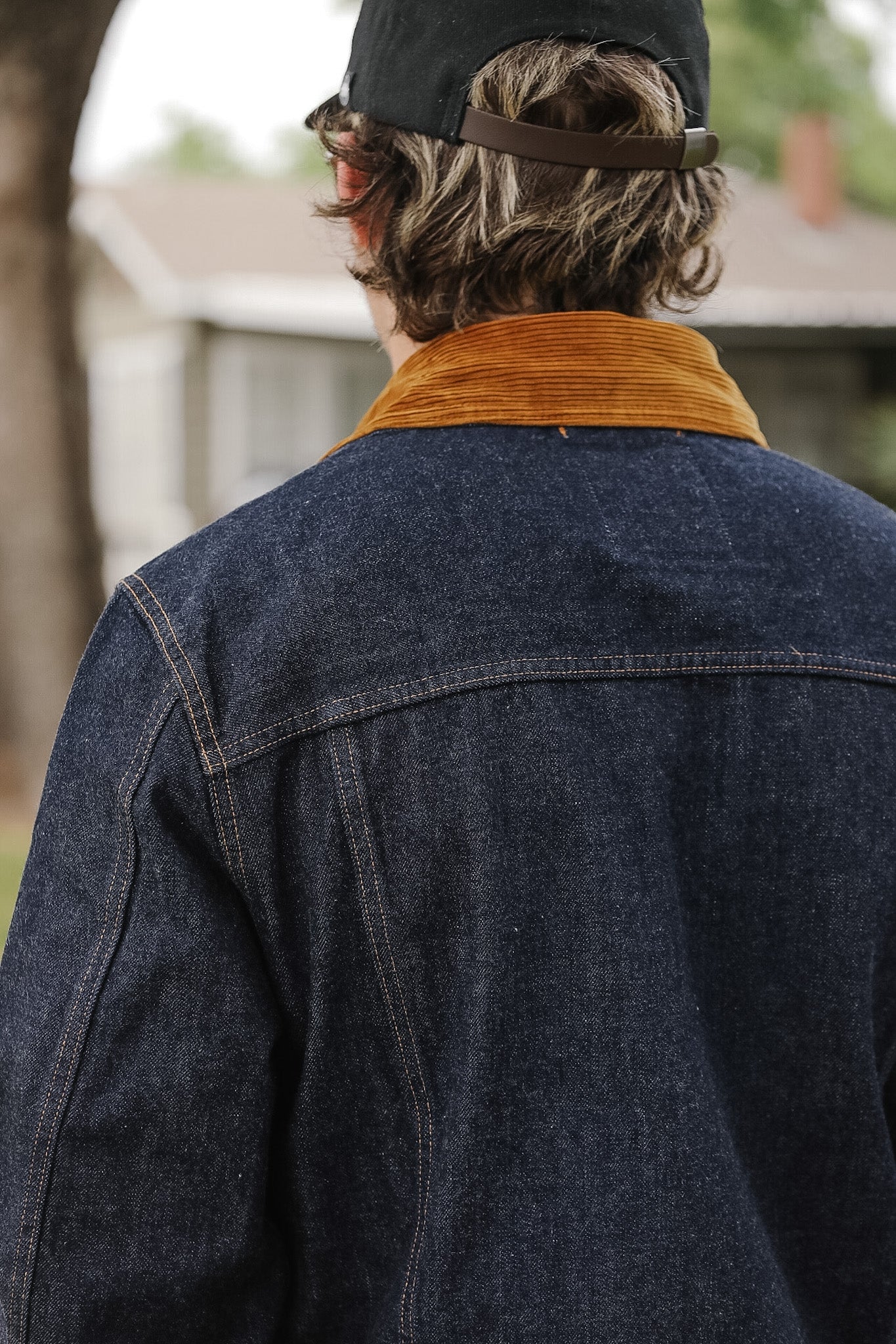 Person wearing a dark denim jacket with a brown corduroy collar, standing outdoors.