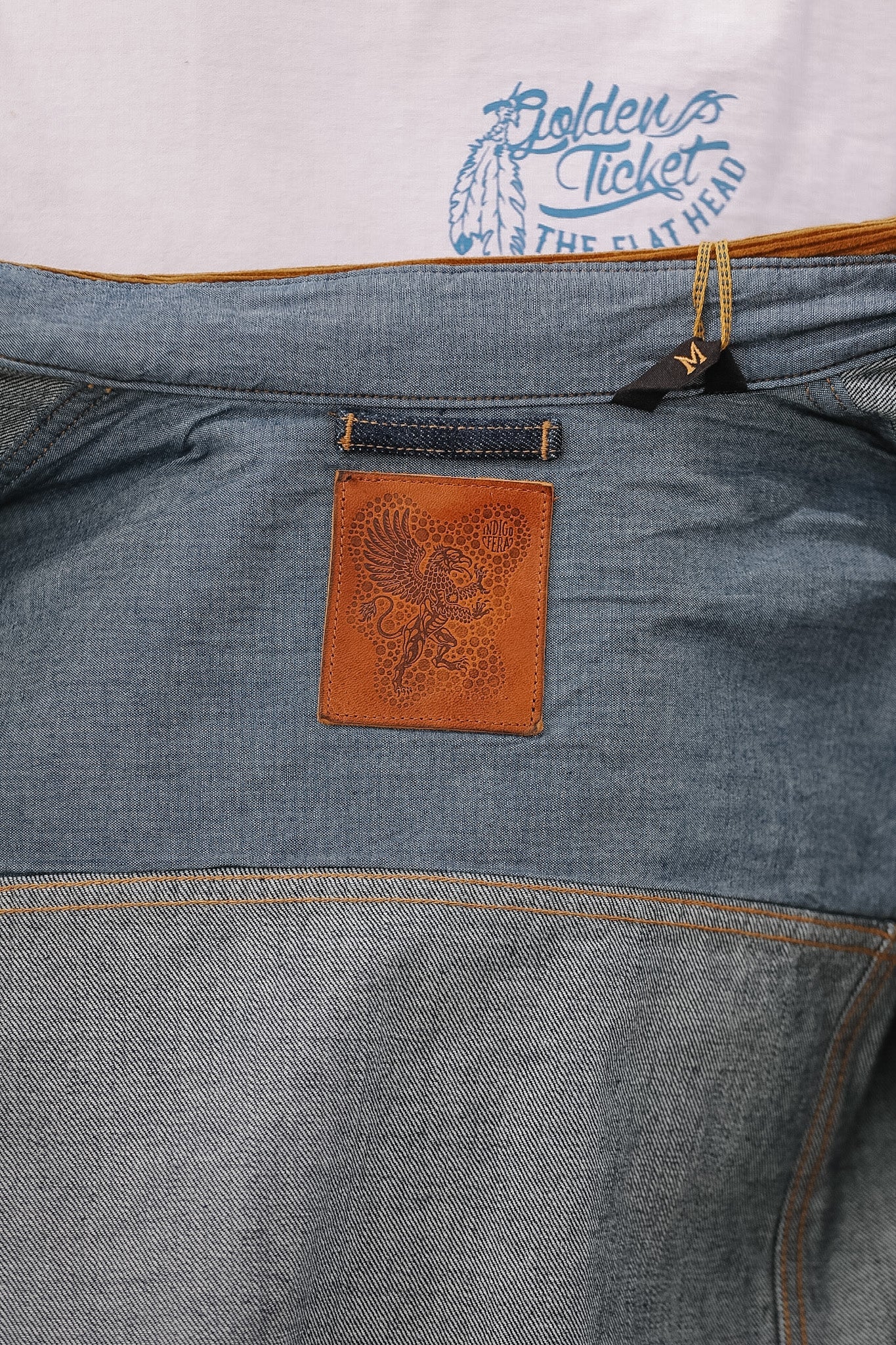 Close-up of a blue denim jacket with a leather patch and 'Golden Ticket' branding.