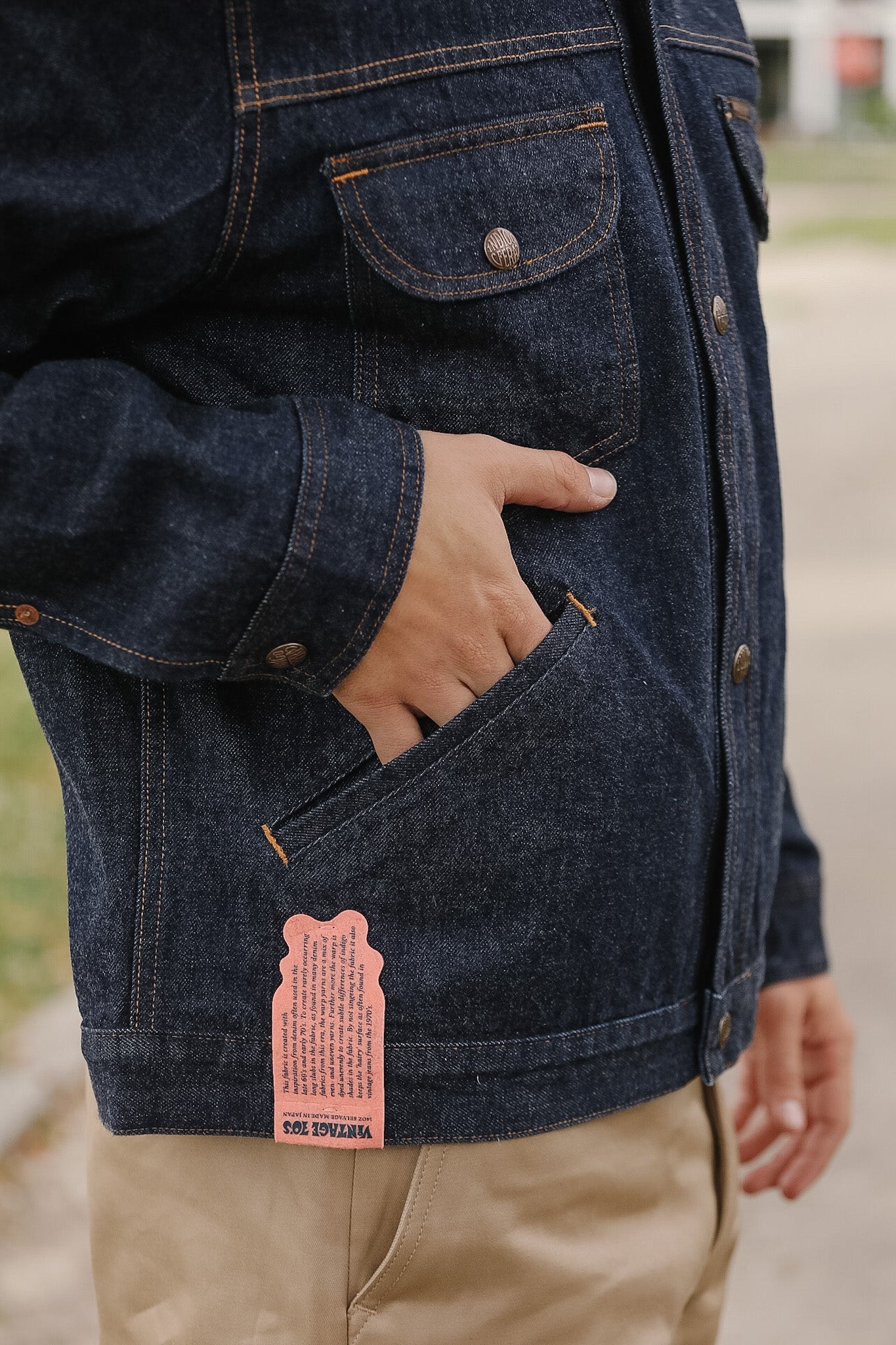 Person wearing a dark denim jacket with a pink tag, standing outdoors.