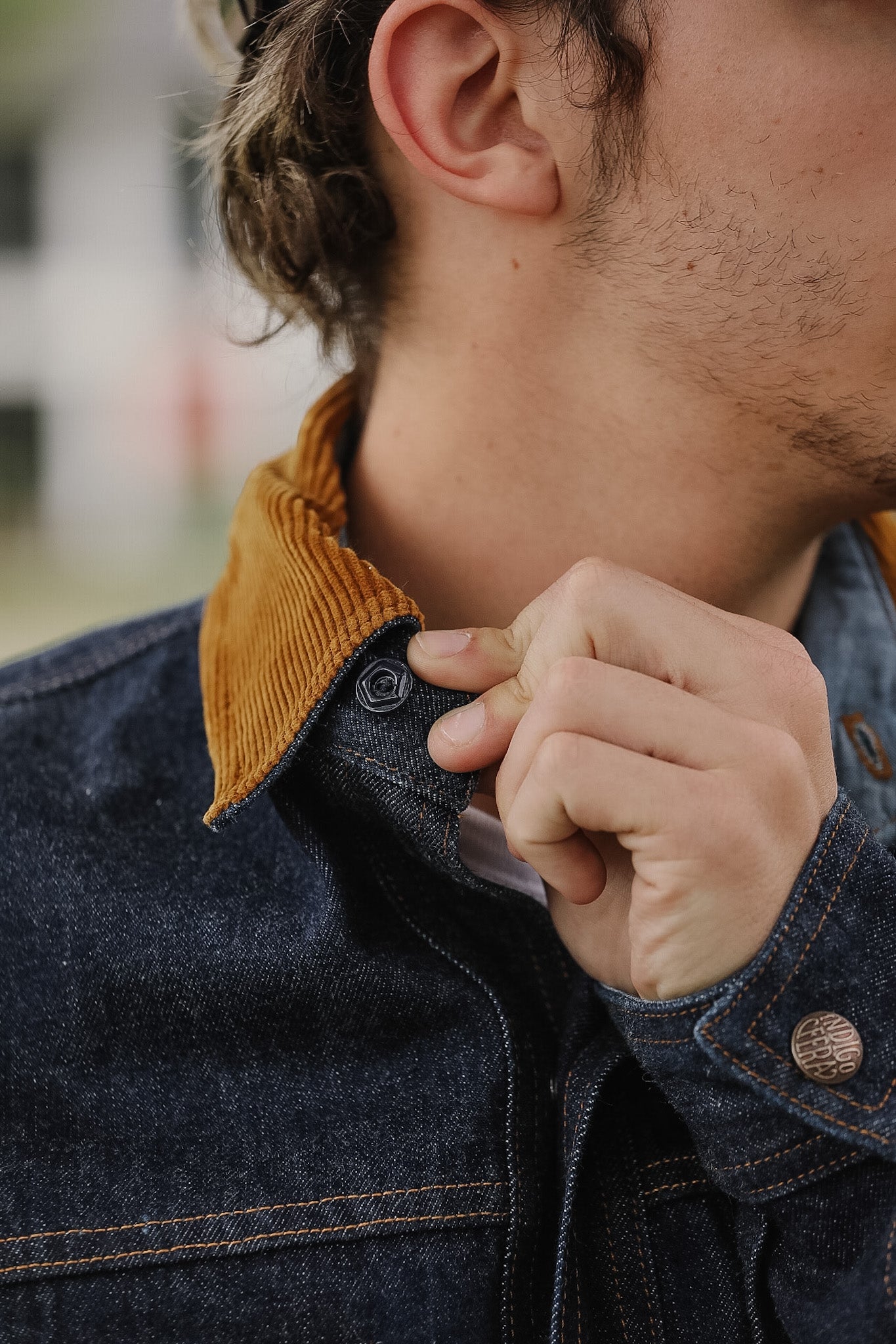 Close-up of a person adjusting the collar of a denim jacket with a mustard-colored inner lining.