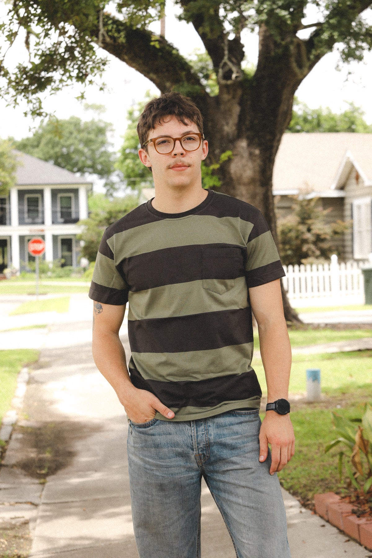 Person wearing a striped shirt standing outdoors with trees and houses in the background