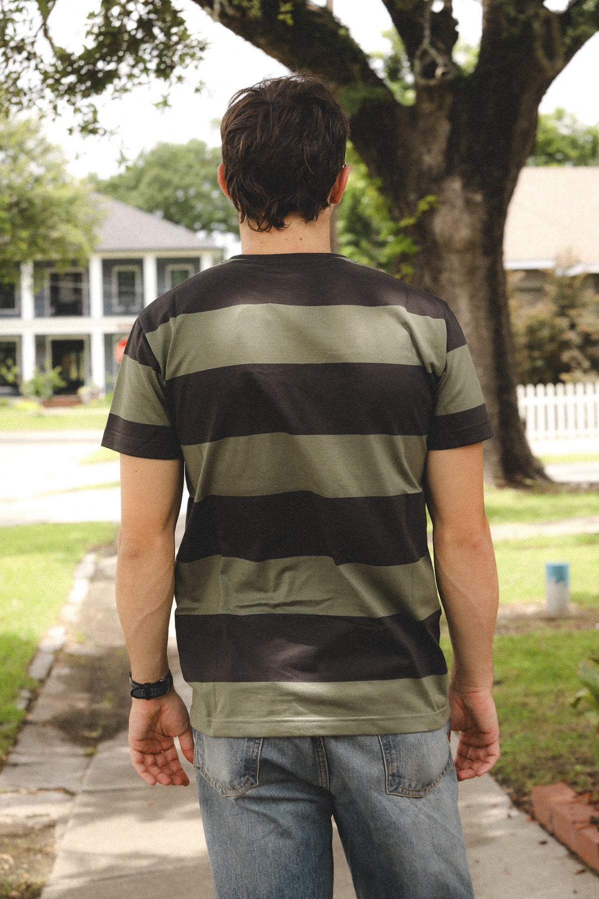 Person wearing a striped shirt standing on a sidewalk with trees and houses in the background