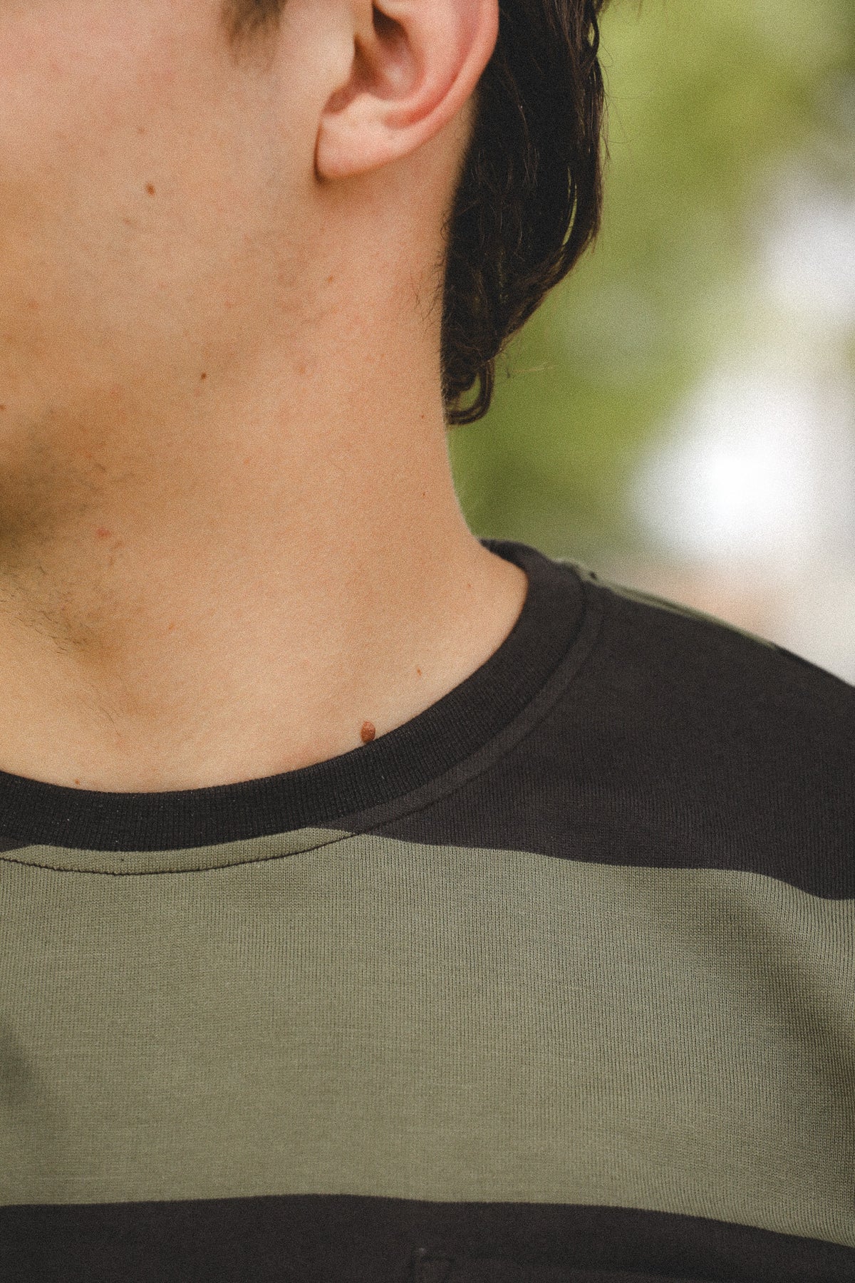 Close-up of a person wearing a green and black striped shirt with a blurred natural background