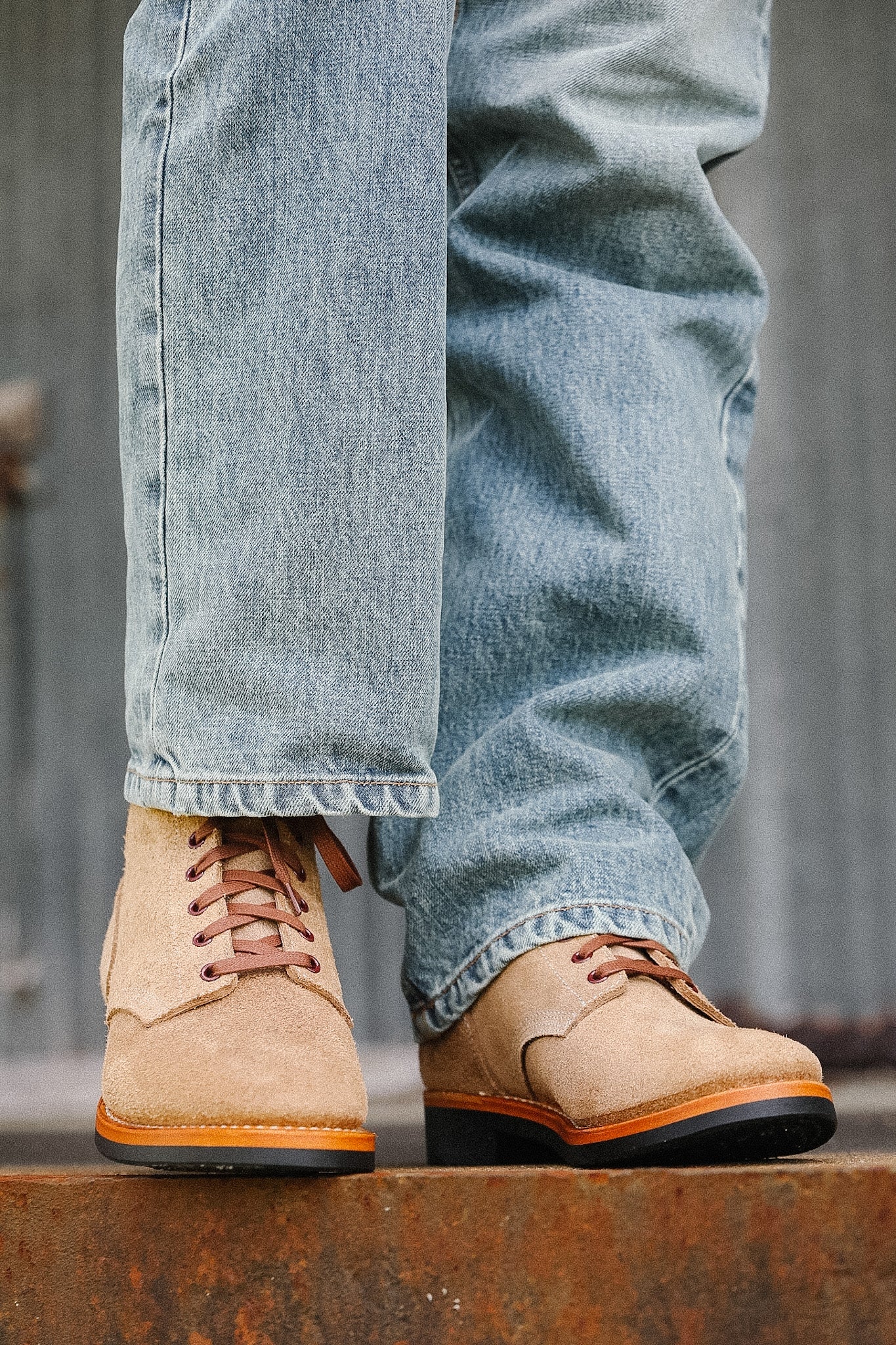 Beige work boots with orange soles worn with light blue jeans on a wooden surface.