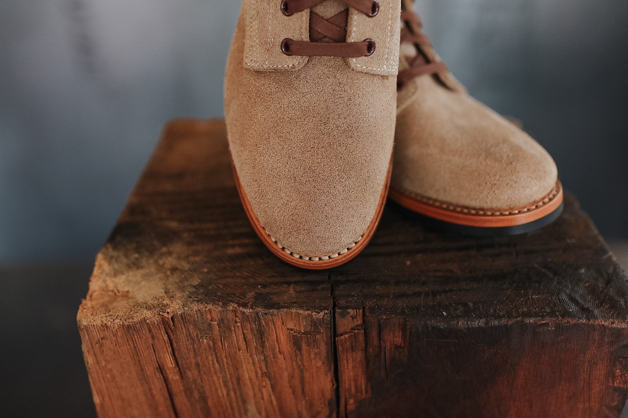 Pair of beige suede shoes on a wooden block with a blurred background