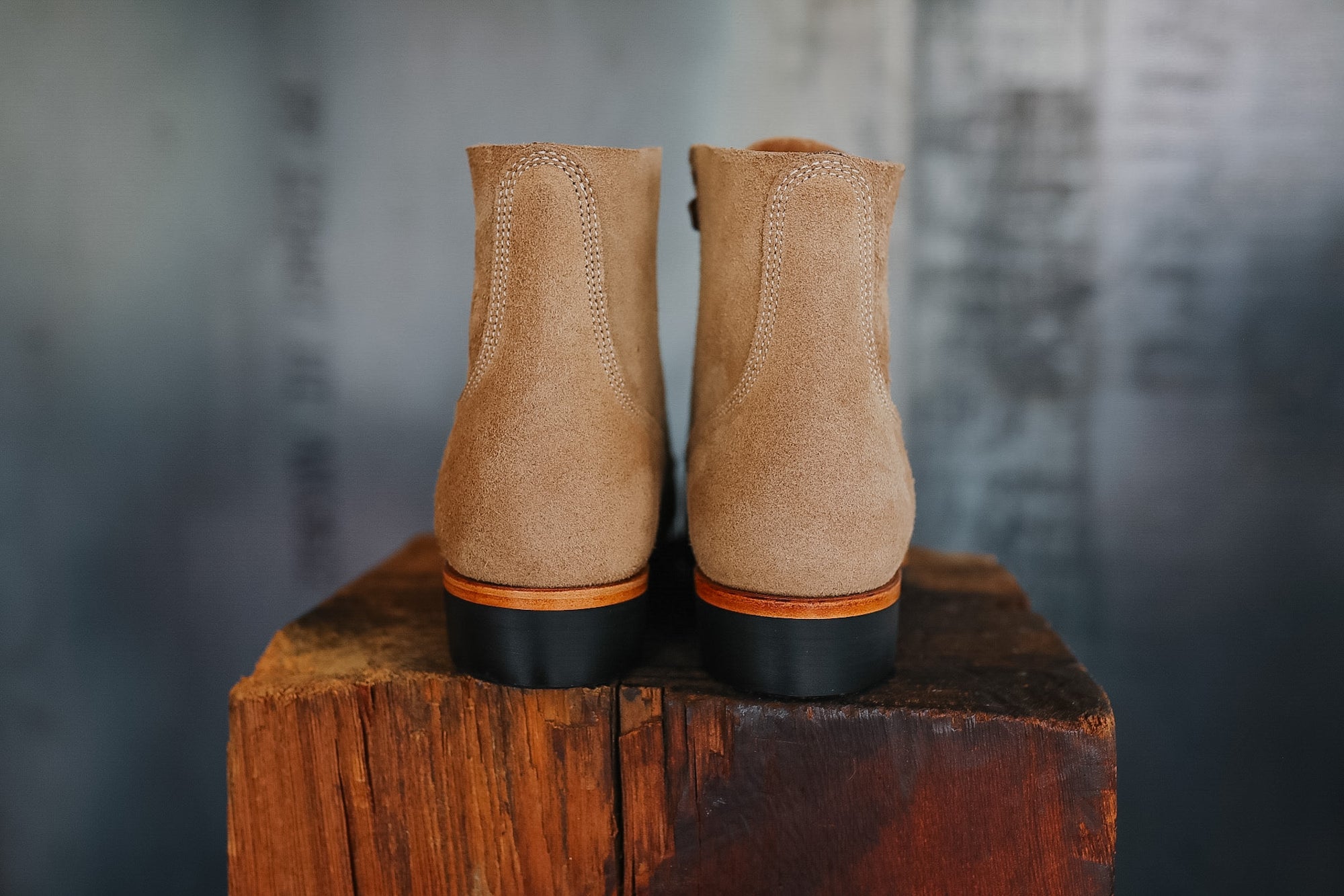 Pair of tan boots with black soles on a wooden block against a gray background
