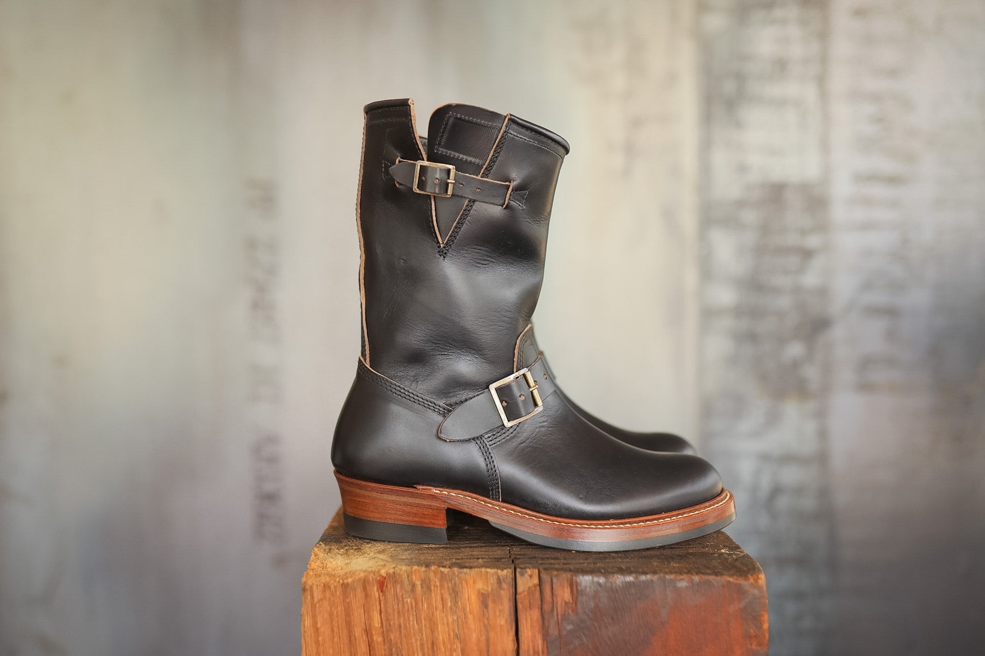 Black leather boot with a buckle on a wooden block against a textured gray background