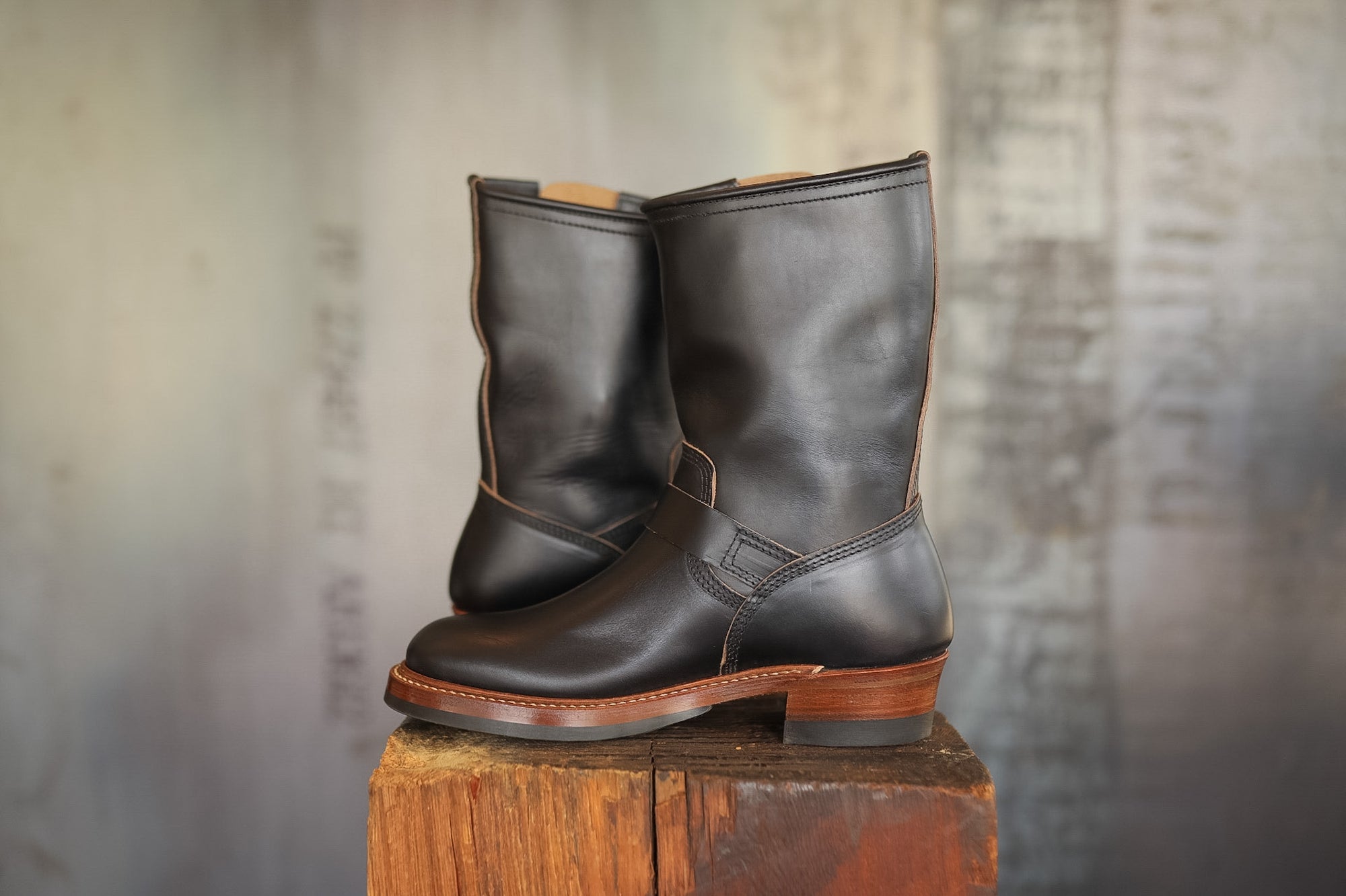 Pair of black leather boots on a wooden block with a textured gray background
