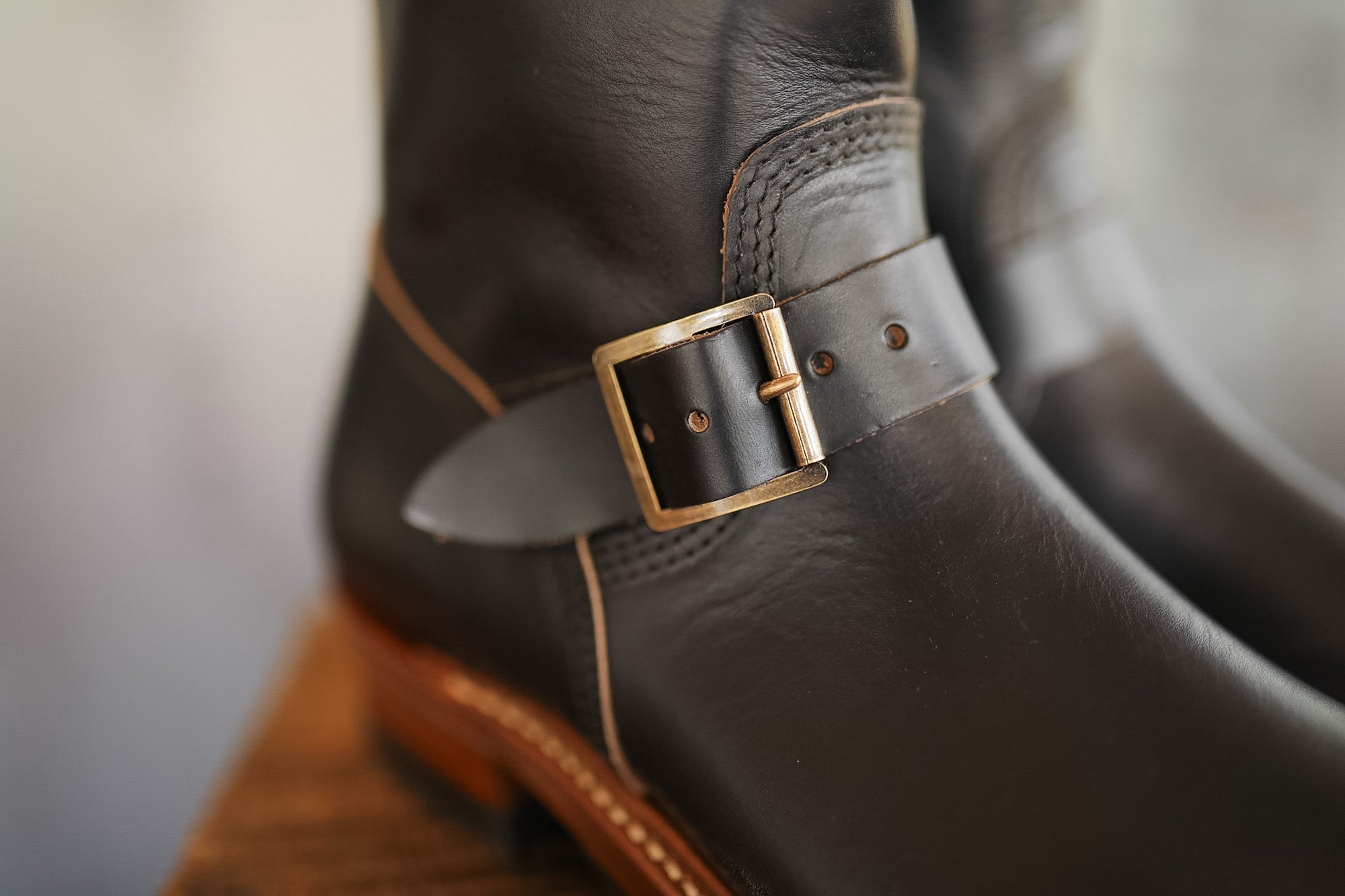 Close-up of a black leather boot with a gold buckle on a blurred background
