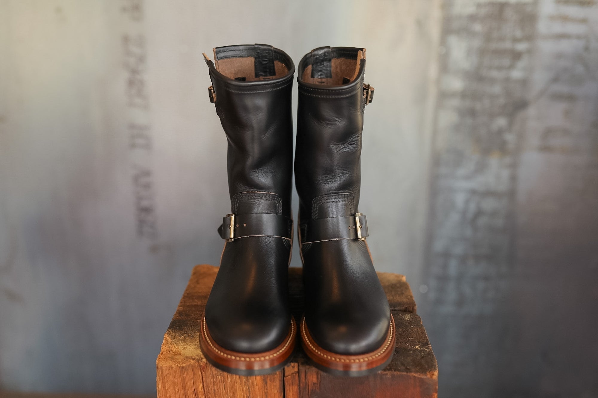 Pair of black leather boots on a wooden block with a textured gray background