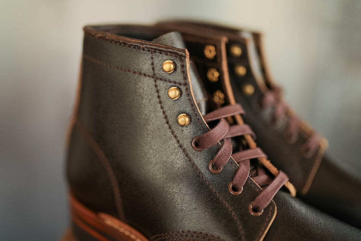 Close-up of brown leather boots with gold buttons on a blurred background