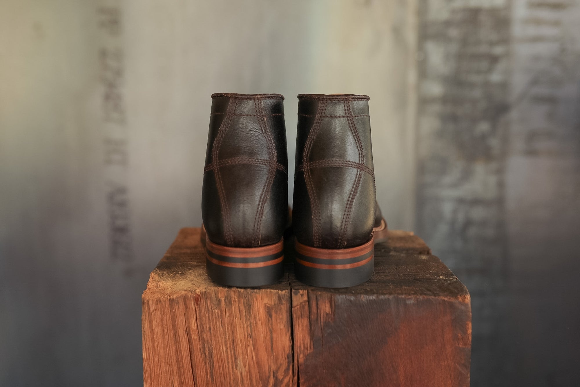 Pair of brown leather boots on a wooden block with a textured wall background