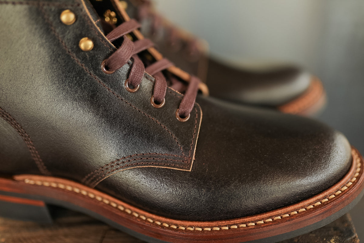 Close-up of brown leather boots with gold buttons on a blurred background
