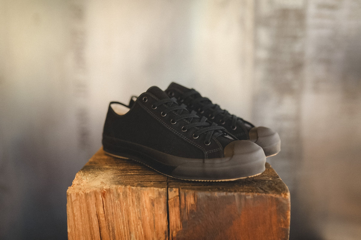 Up close image of a black sneaker on a wood block with a grey background 