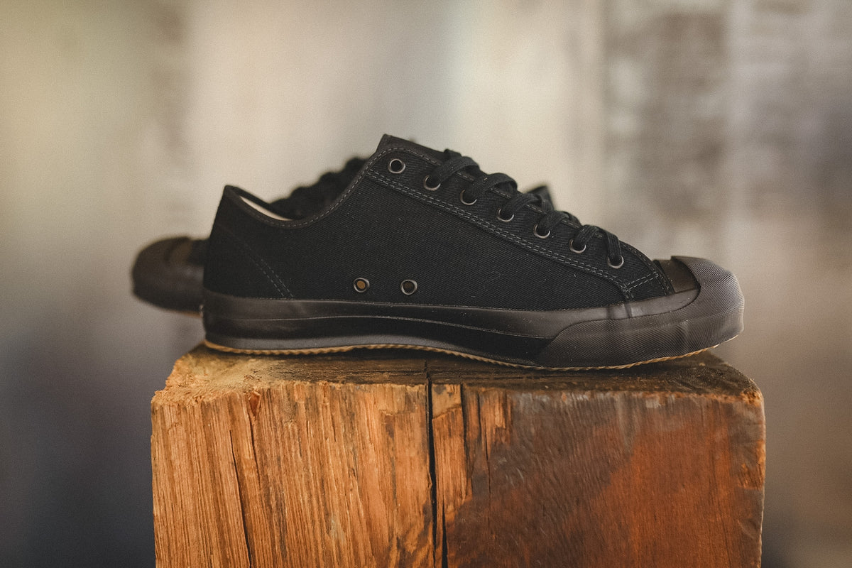 Up close image of a black sneaker on a wood block with a grey background 