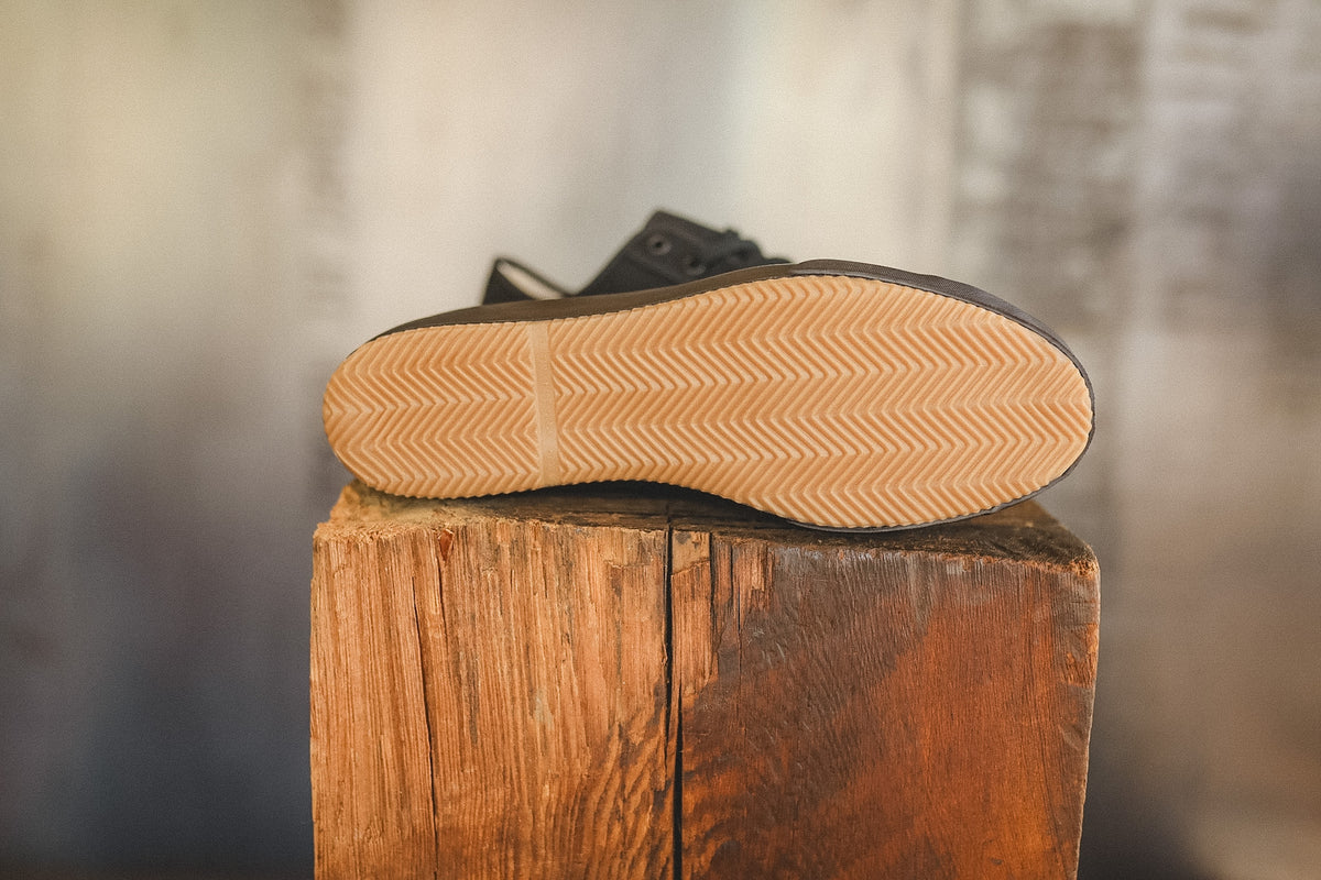 Up close image of a black sneaker on a wood block with a grey background 