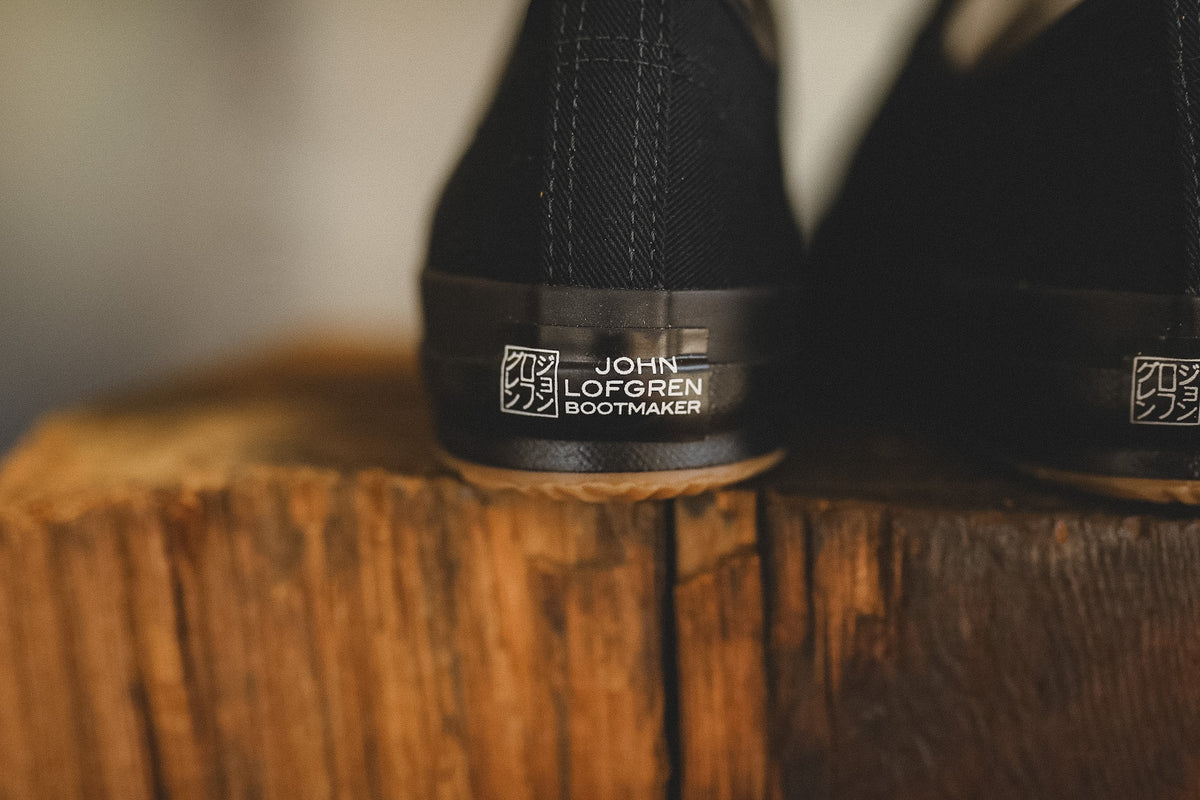 Up close image of a black sneaker on a wood block with a grey background 