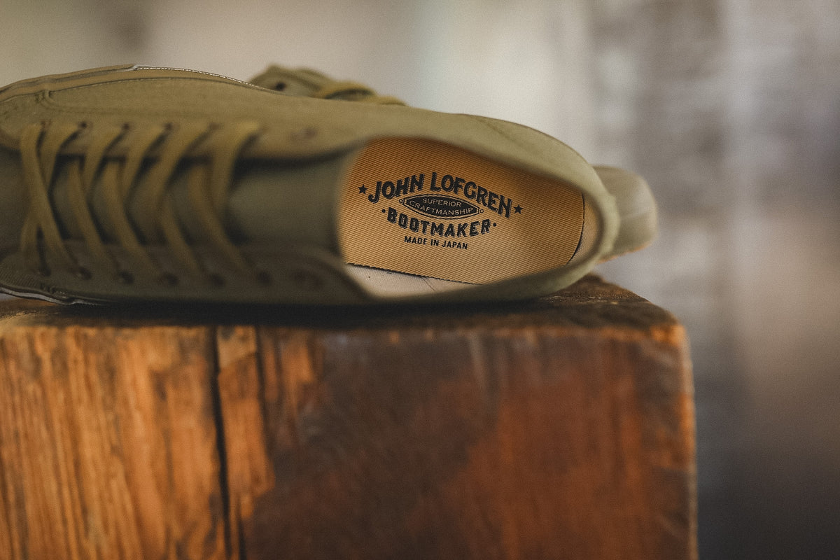 Up close image of a olive green sneaker on a wood block with a grey background 