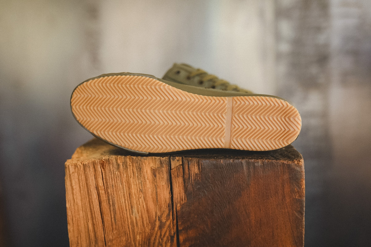 Up close image of a olive green sneaker on a wood block with a grey background 