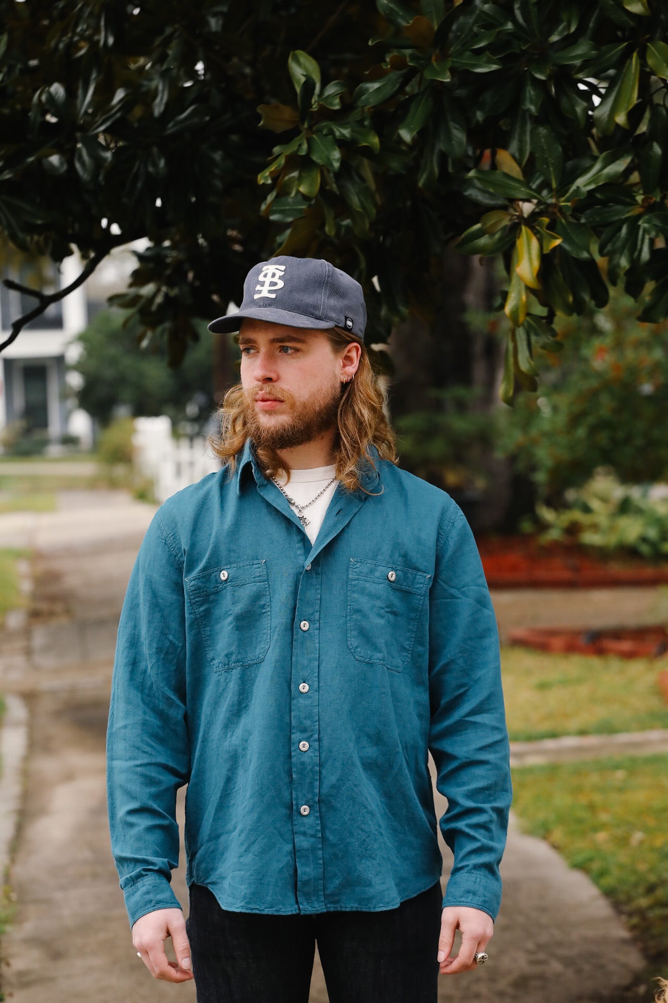 Man wearing a blue shirt and cap standing outdoors with trees in the background