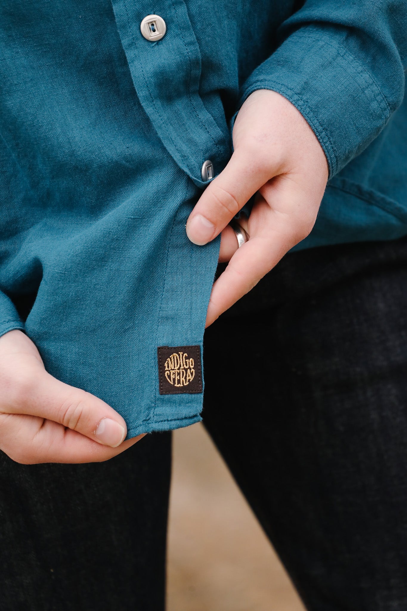 Close-up of a person wearing a teal shirt with a brand logo on the sleeve.