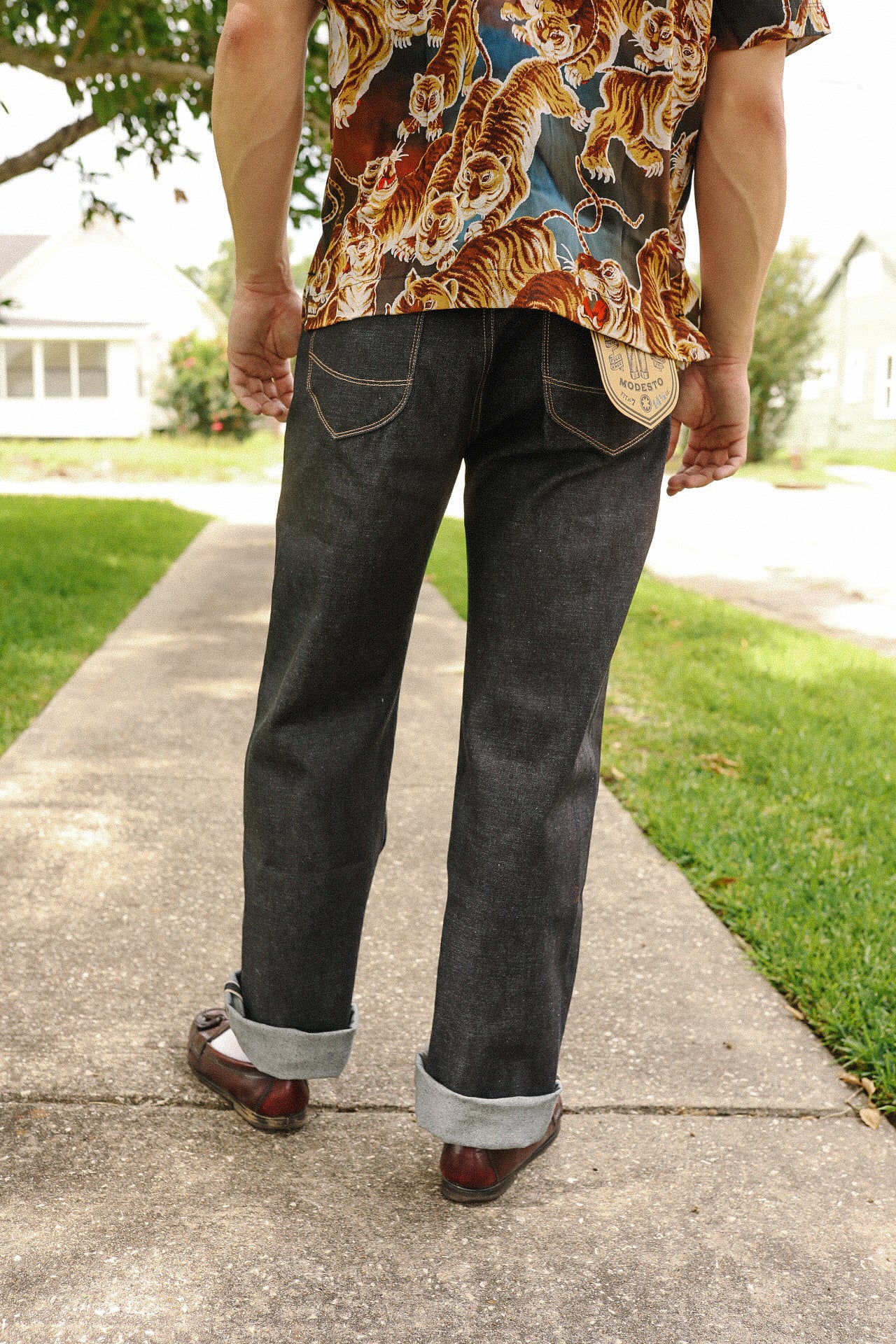 Person wearing dark raw denim jeans cuffed at ankles and a tiger pattern shirt walking on sidewalk