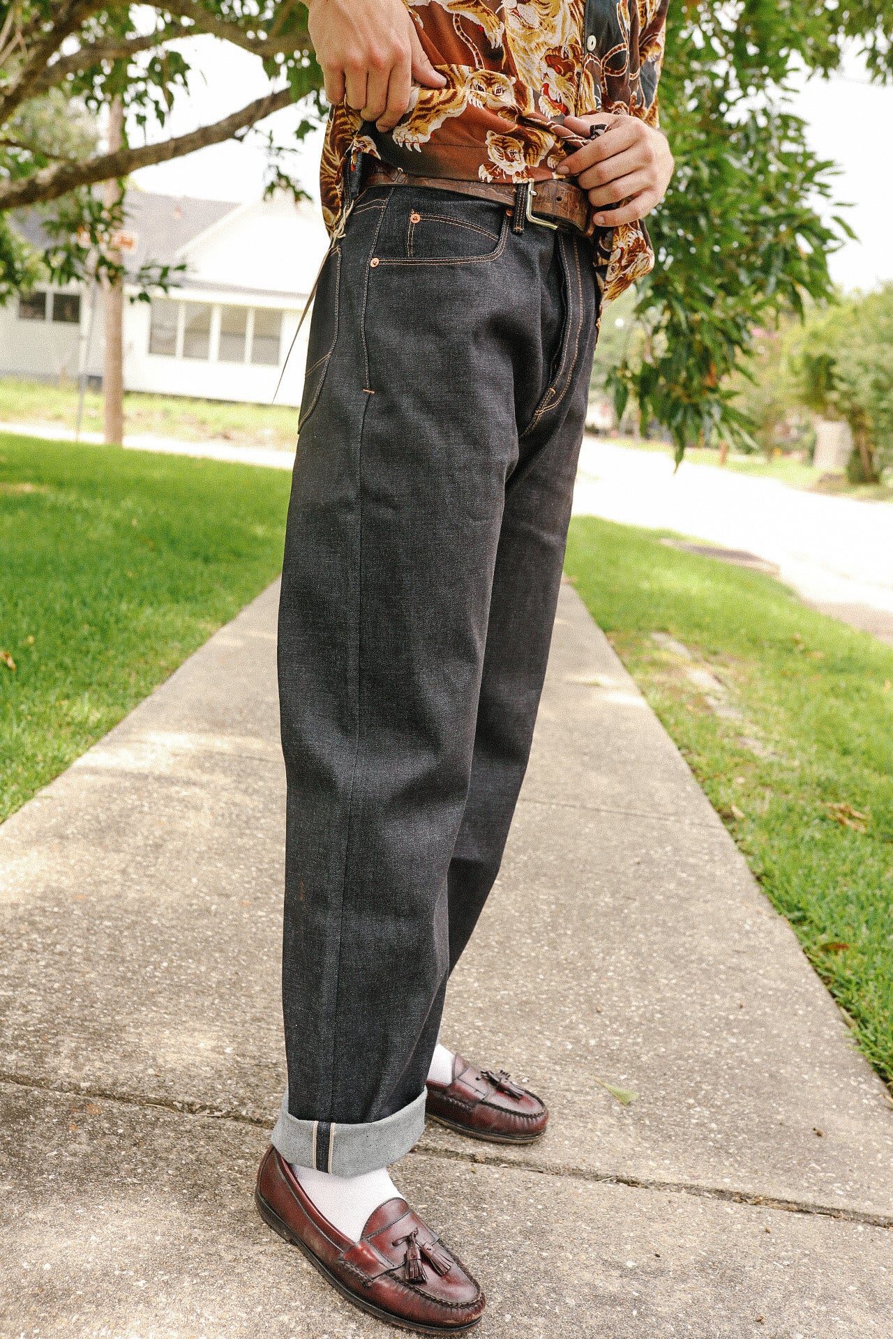 Person wearing dark indigo rolled-up Kaihara denim jeans, brown tassel loafers, and printed shirt outdoors