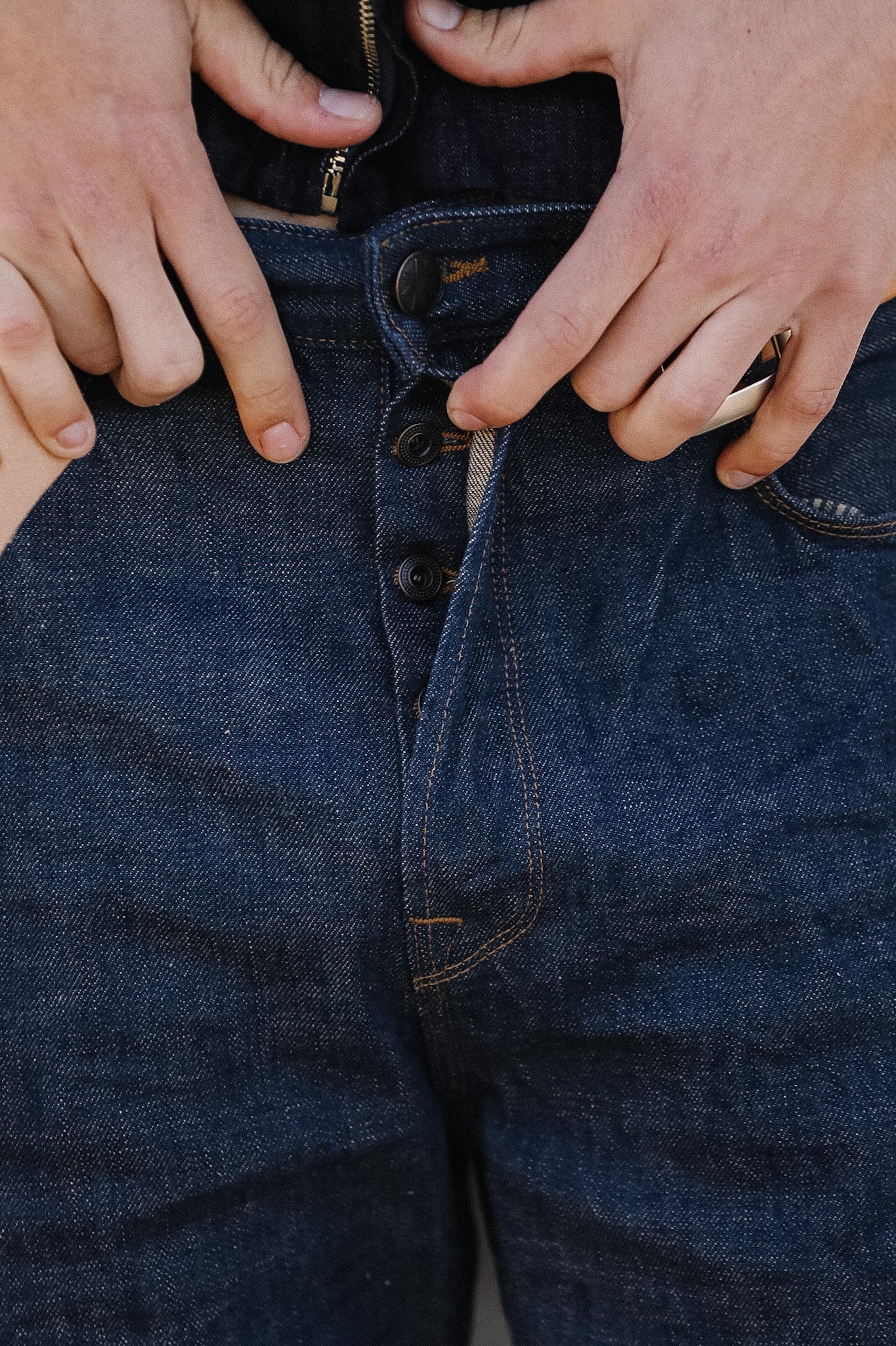 Close-up of hands buttoning a blue denim jacket